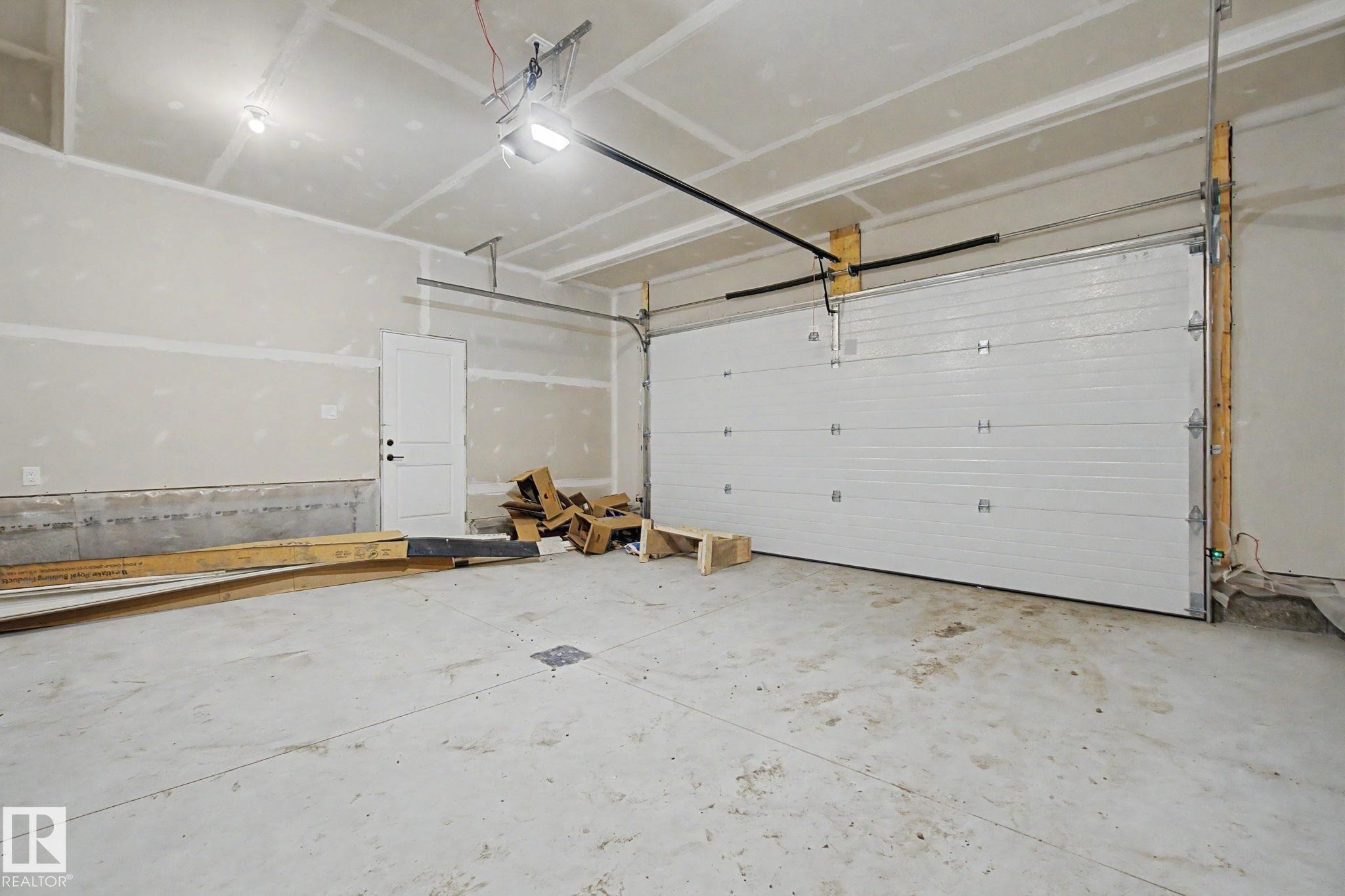 Spacious garage featuring a concrete floor, white paneled garage door, and a single interior door - 4 Willow Heights Drive, Stony Plain, AB