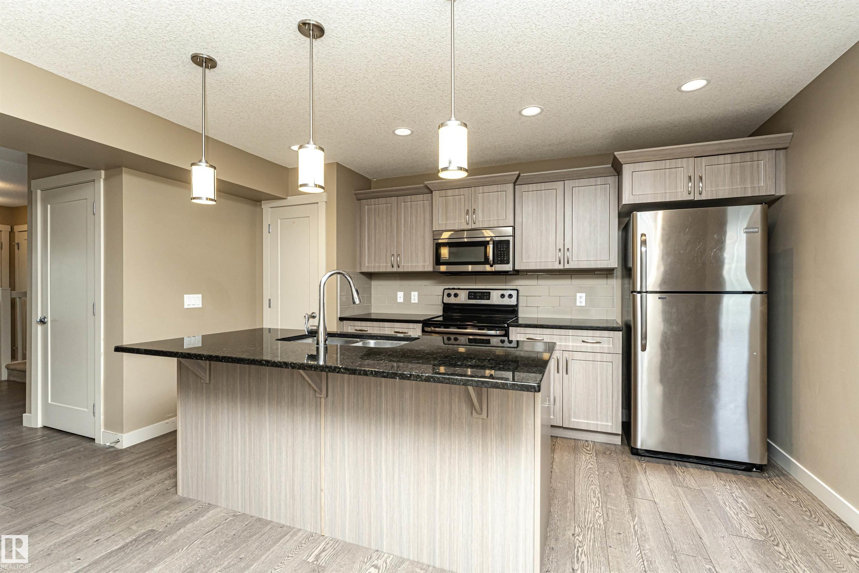 Modern kitchen featuring a granite-topped island with pendant lighting, stainless steel appliances, light wood-finish cabinetry, and wood-finish flooring - 2397 Glenridding Boulevard, Edmonton, AB