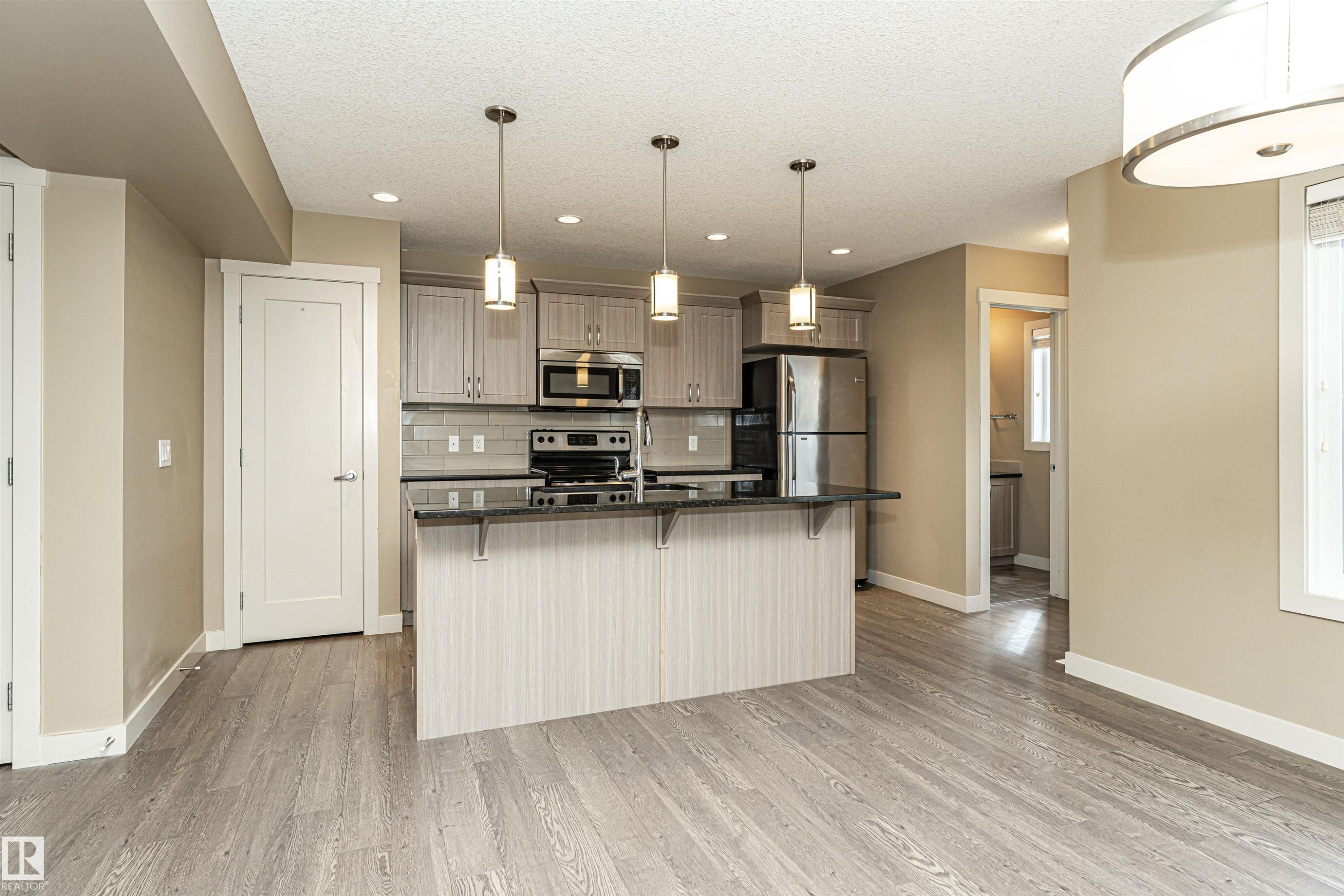 Open-concept kitchen featuring light-toned cabinetry, stainless steel appliances, a breakfast bar island with pendant lighting, and grey subway tile backsplash - 2397 Glenridding Boulevard, Edmonton, AB