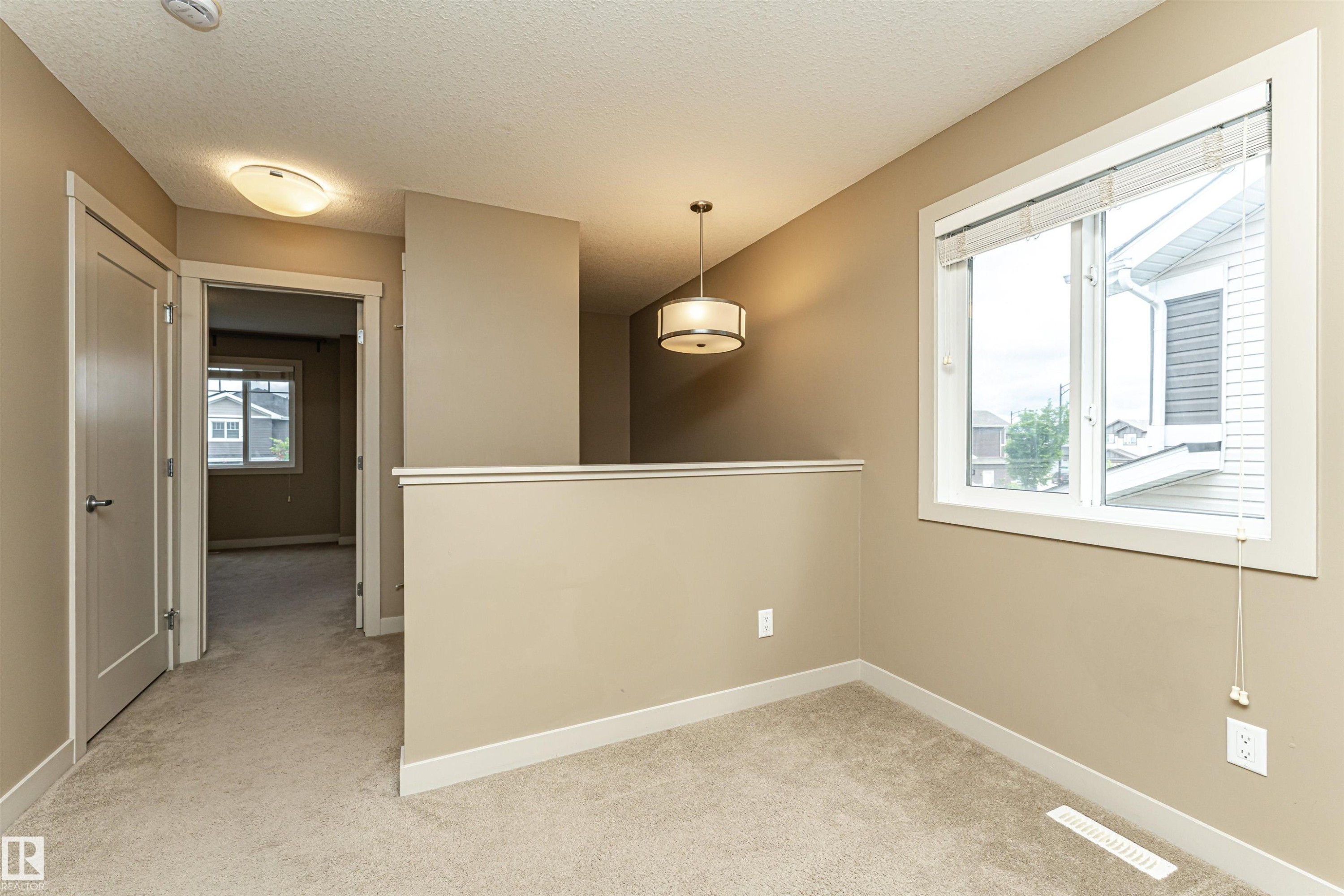 Carpeted upper-level landing featuring a large window, a semi-flush mount light fixture, a modern drum pendant light, and a white railing - 2397 Glenridding Boulevard, Edmonton, AB