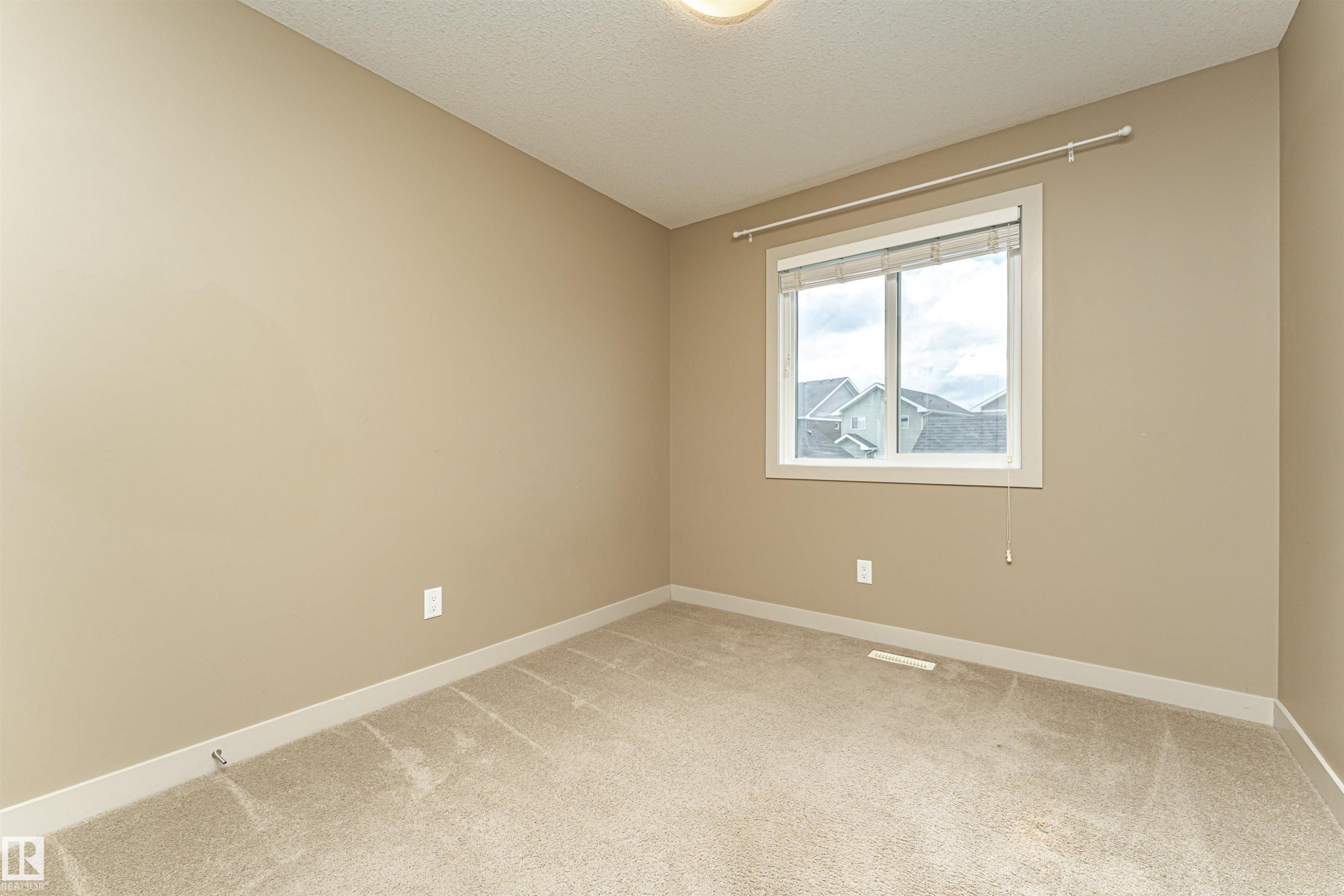 Neutral-toned walls and carpeted flooring define this room, featuring a double-paned window with a white frame and blinds - 2397 Glenridding Boulevard, Edmonton, AB