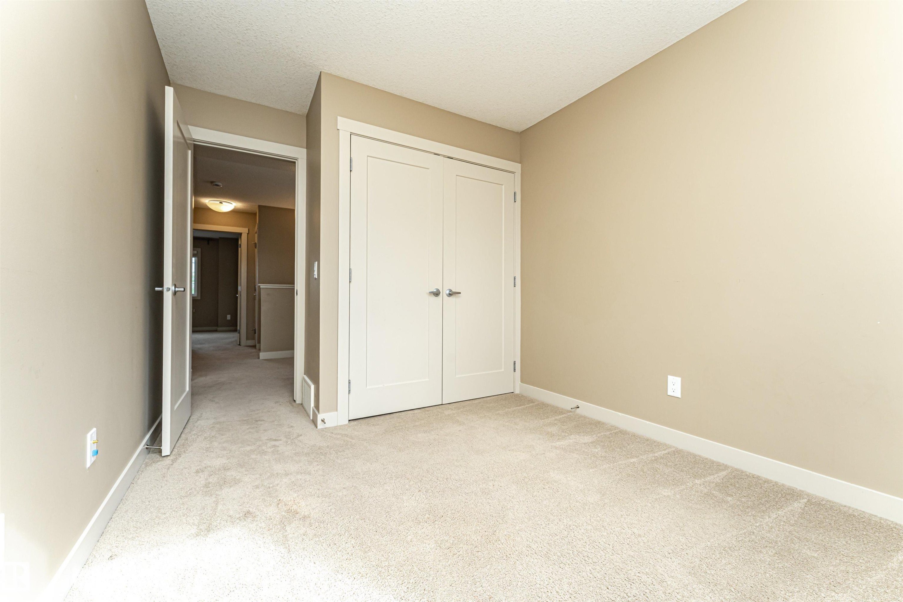 Neutral tone walls with white trim, light-colored carpet flooring, and a double-door closet with brushed nickel hardware - 2397 Glenridding Boulevard, Edmonton, AB