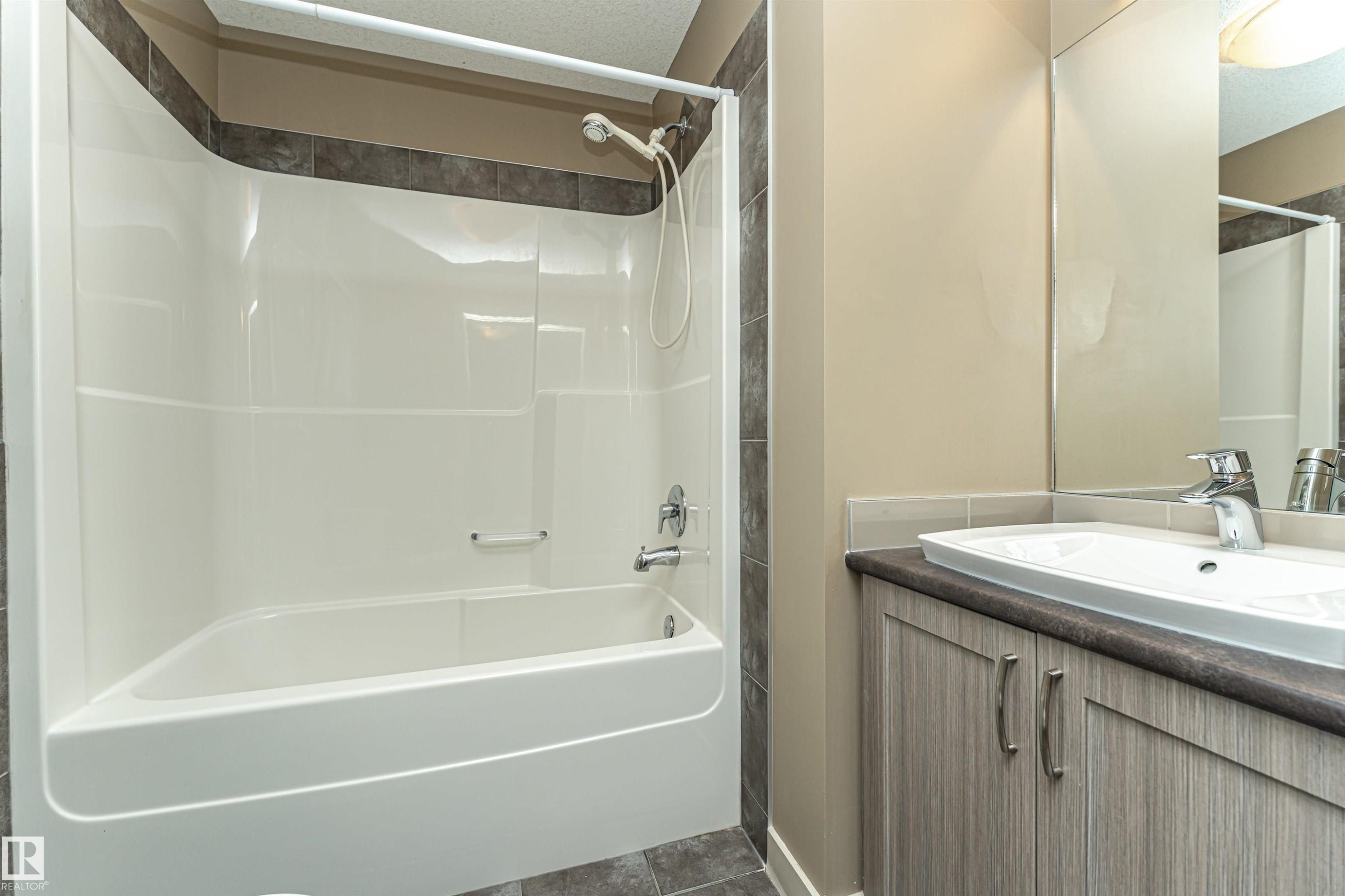 Bathroom featuring a white tub and shower combination with dark tile surround - 2397 Glenridding Boulevard, Edmonton, AB