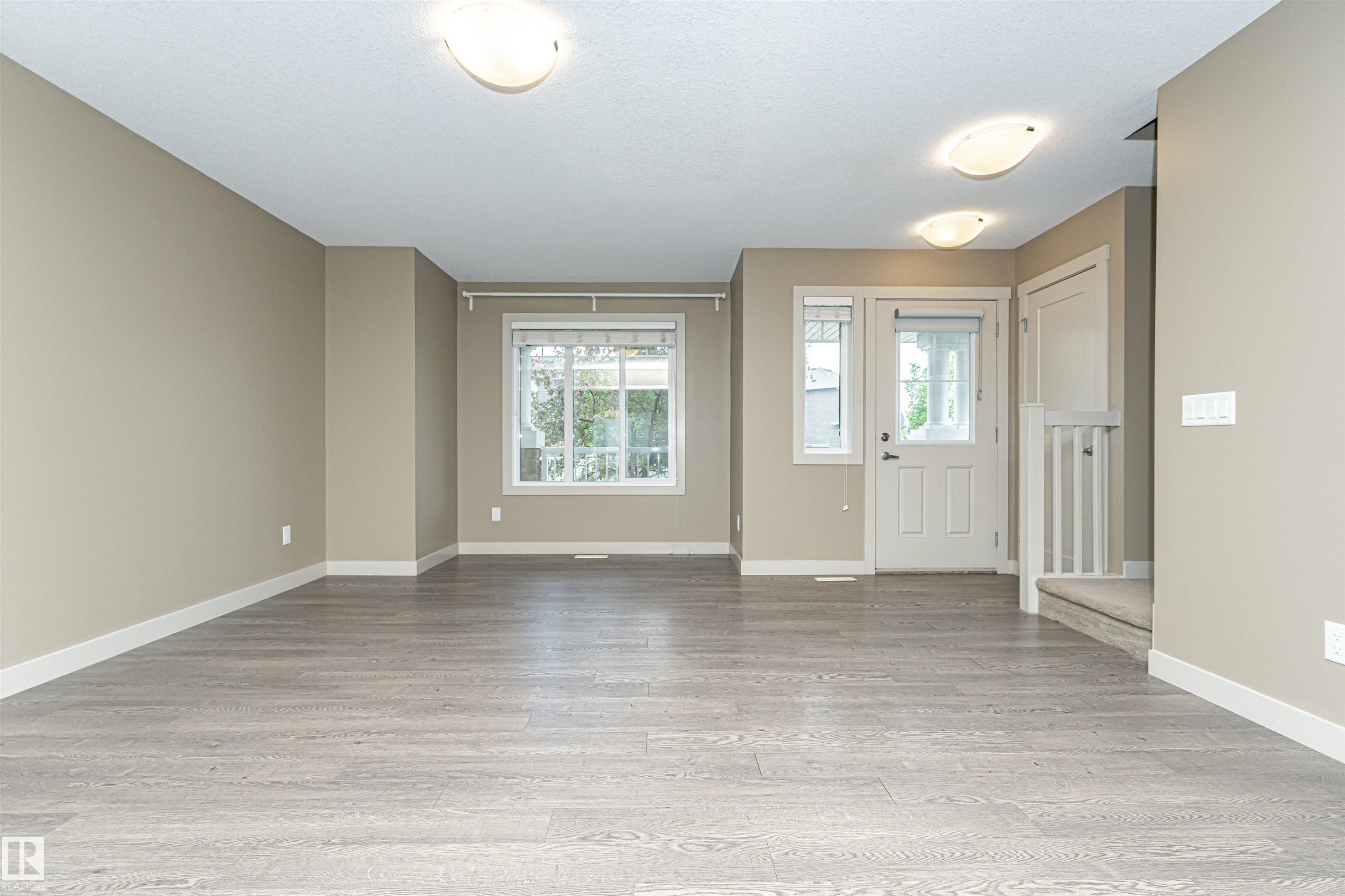 Spacious interior featuring wood-finish flooring, neutral wall tones, white trim, and ample natural light from multiple windows - 2397 Glenridding Boulevard, Edmonton, AB