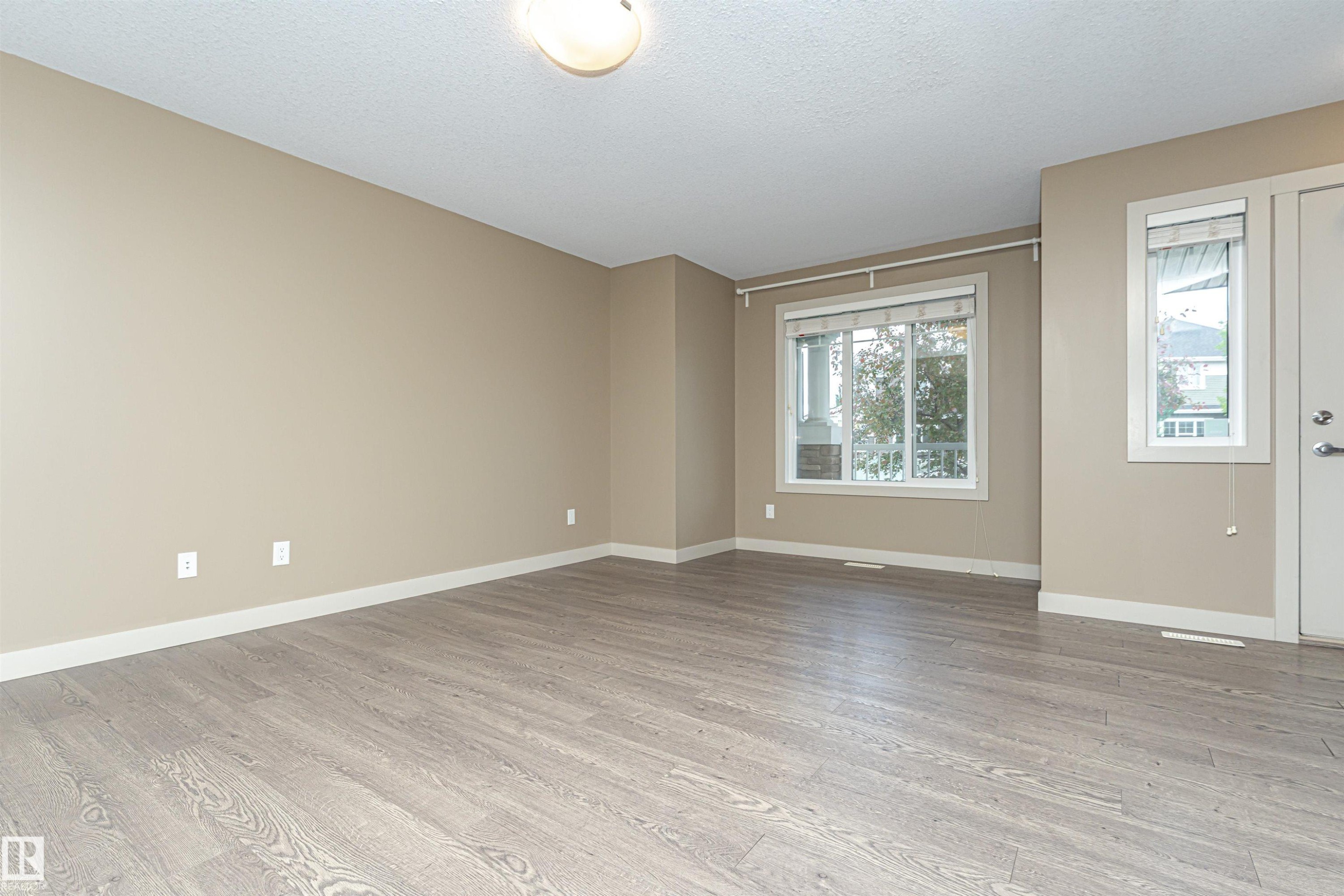 Spacious room featuring wood-finish flooring, neutral-toned walls, and white baseboards - 2397 Glenridding Boulevard, Edmonton, AB