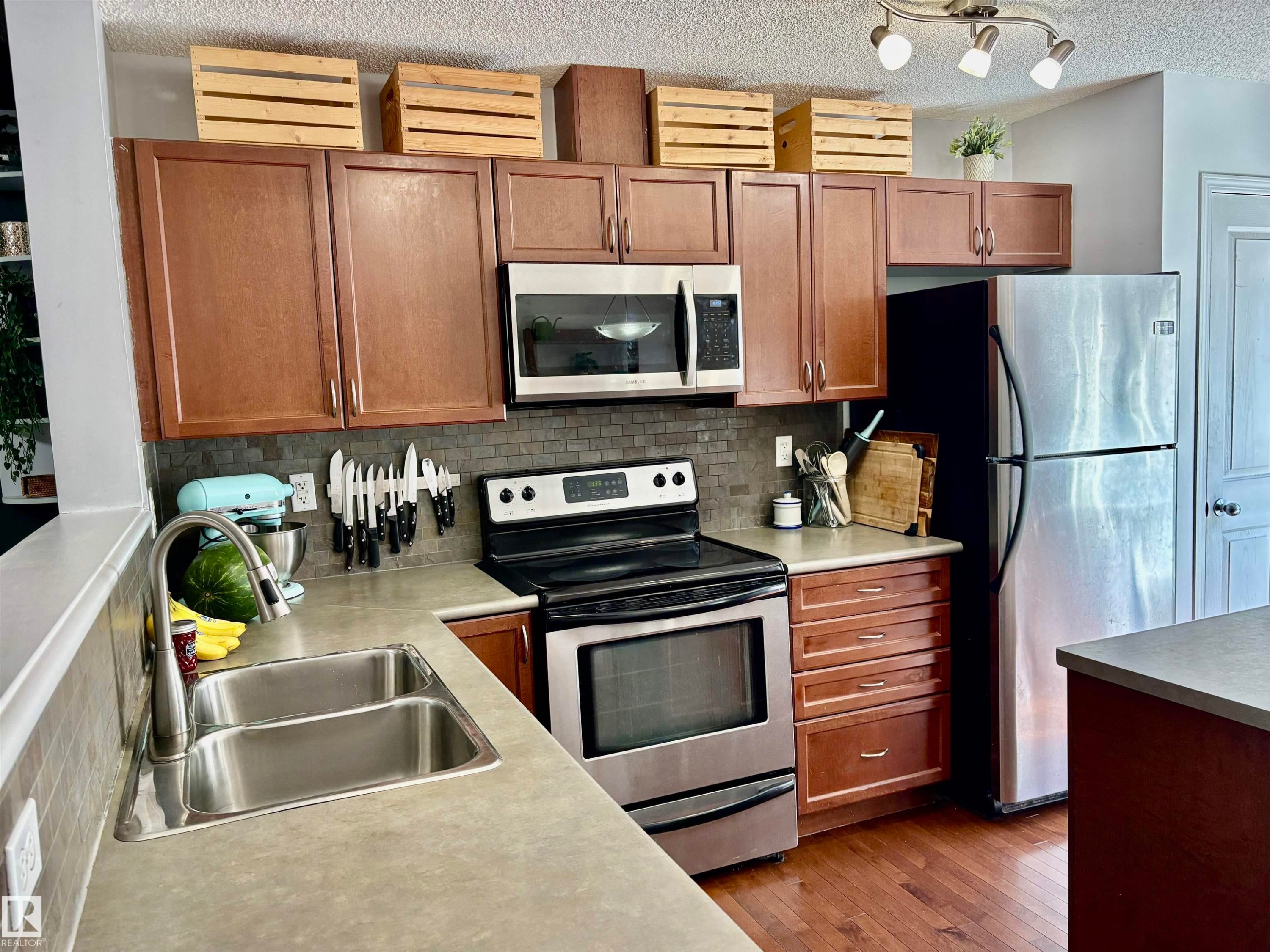 Kitchen featuring wood-finish cabinetry, stainless steel appliances, a grey mosaic tile backsplash, and light-toned countertops - 184 1804 70 Street, Edmonton, AB
