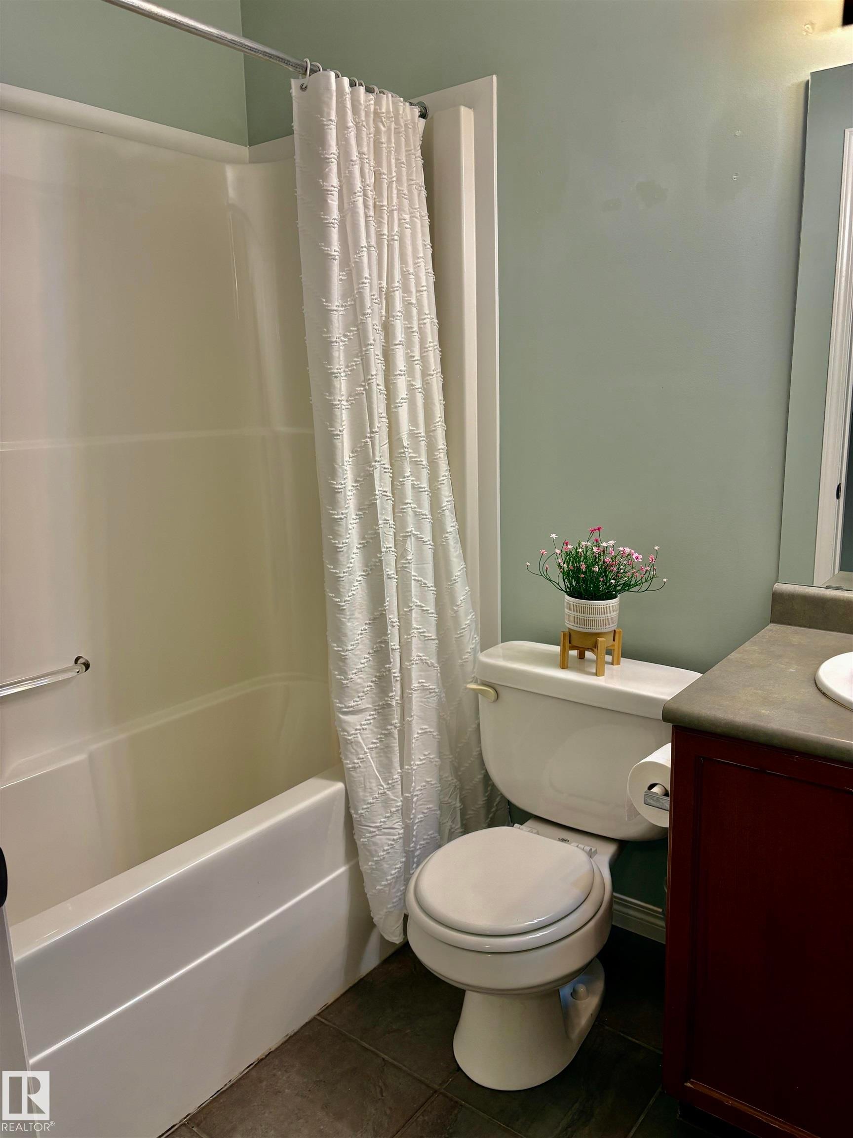 Bathroom featuring a white tub/shower combination with a grab bar, a white toilet, a vanity with a dark countertop, and tile flooring - 184 1804 70 Street, Edmonton, AB