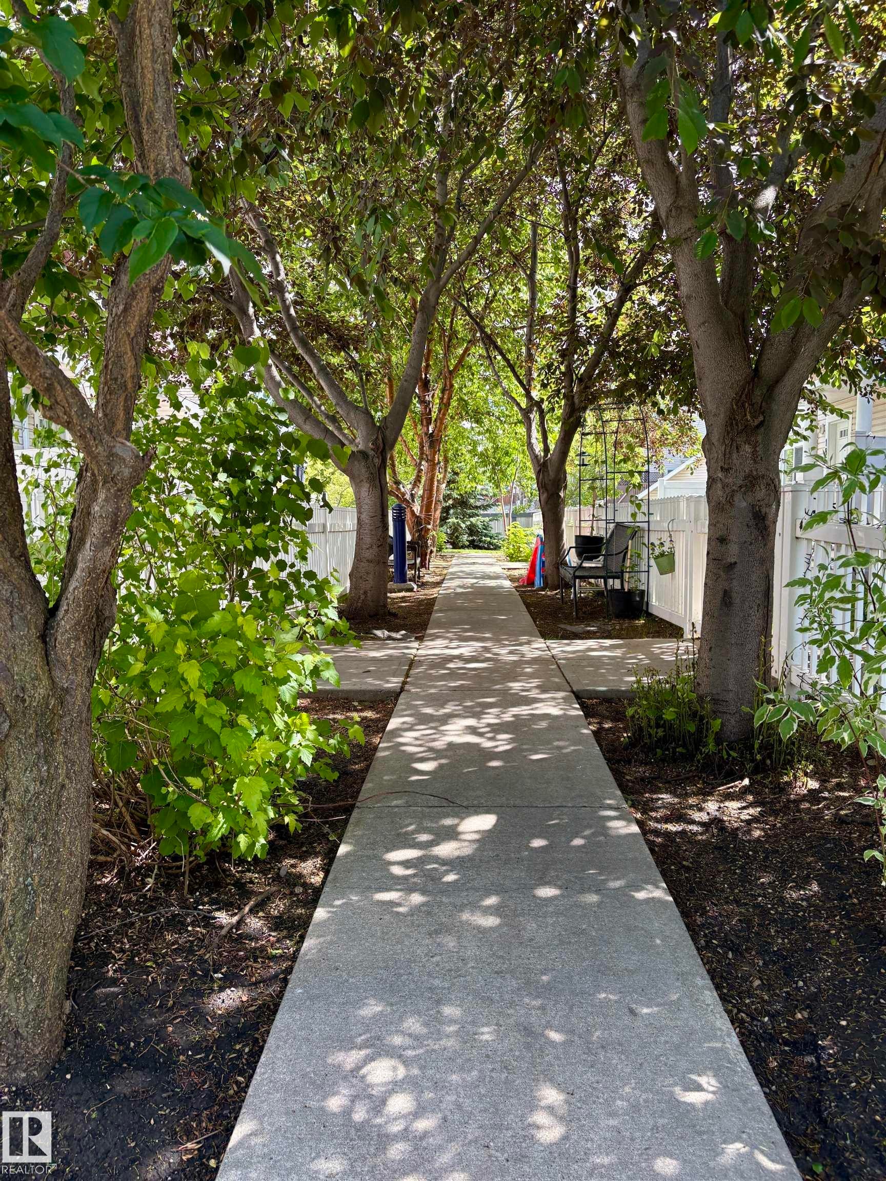 Concrete pathway bordered by mature trees and lush greenery - 184 1804 70 Street, Edmonton, AB