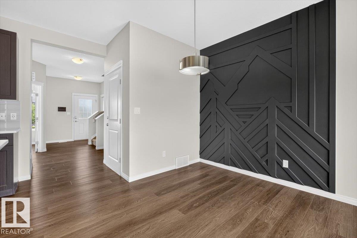 Dining area with a black accent wall featuring geometric paneling, wood-finish flooring, and a contemporary pendant light fixture - 2144 51 Street, Edmonton, AB