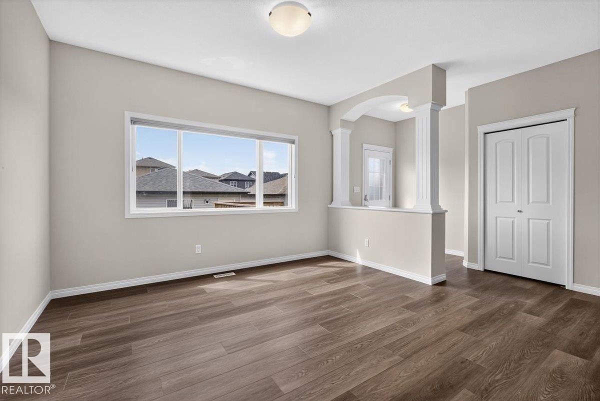 Open concept living area featuring wood-finish flooring, a large window, neutral wall tones, and decorative archways with columns - 2144 51 Street, Edmonton, AB