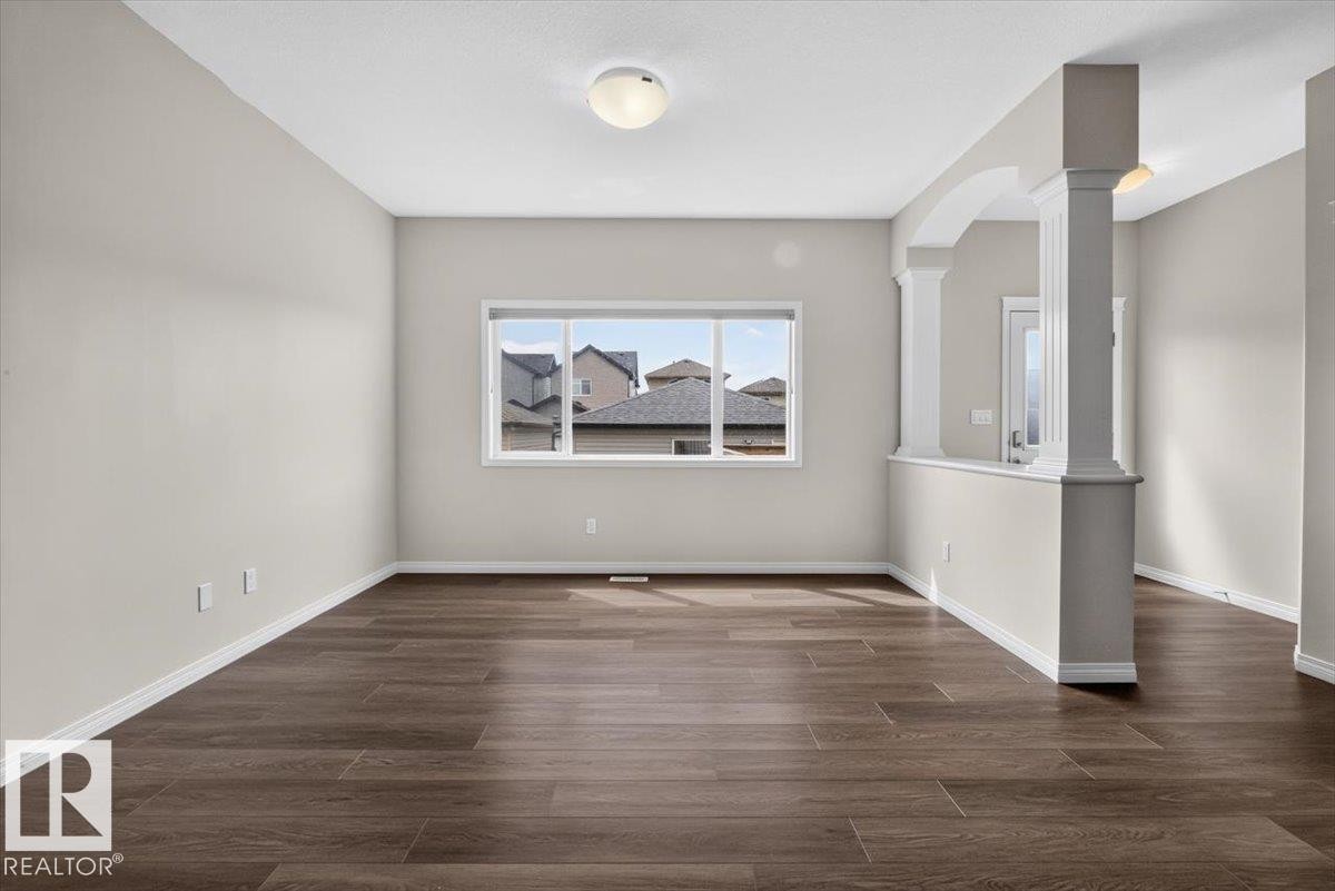 Spacious room featuring wood-finish flooring, neutral-toned walls, and a large window - 2144 51 Street, Edmonton, AB