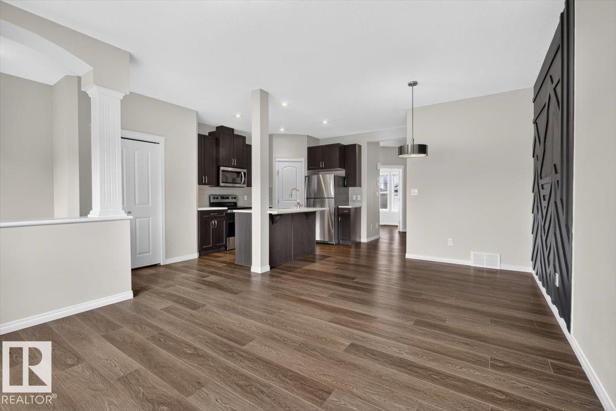 Spacious open-concept living area featuring wood-finish flooring, recessed lighting, and a decorative wall panel - 2144 51 Street, Edmonton, AB