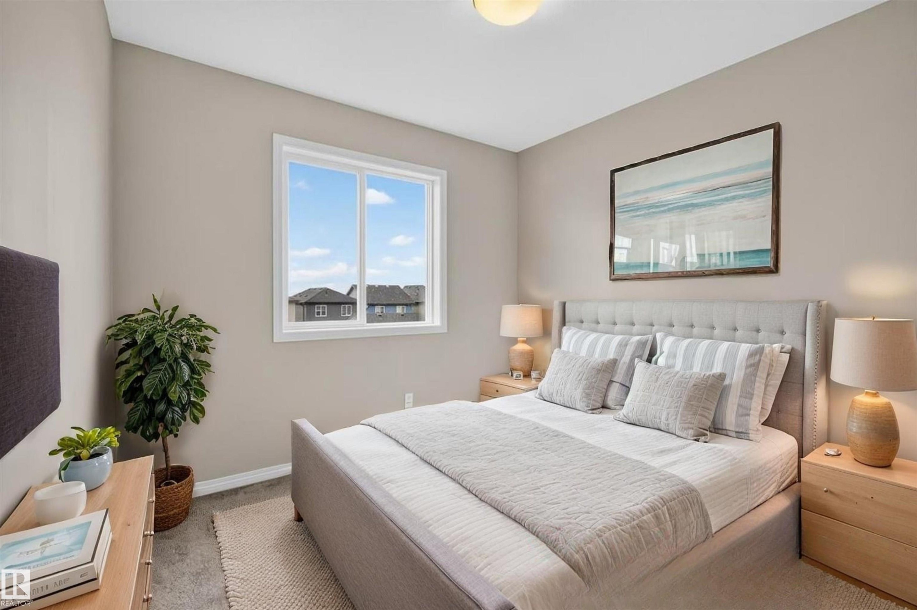 Bedroom featuring a neutral color palette, a large window, a light gray upholstered bed frame, light wood nightstands, and a flush mount ceiling light - 2144 51 Street, Edmonton, AB