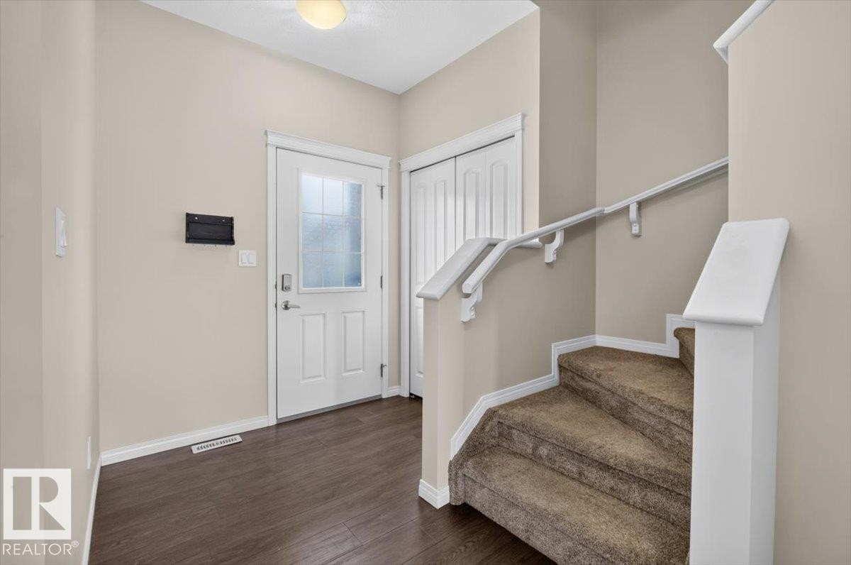 Inviting entryway featuring dark wood-finish flooring, a white front door with decorative glass, white trim, and a carpeted staircase with a white railing - 2144 51 Street, Edmonton, AB