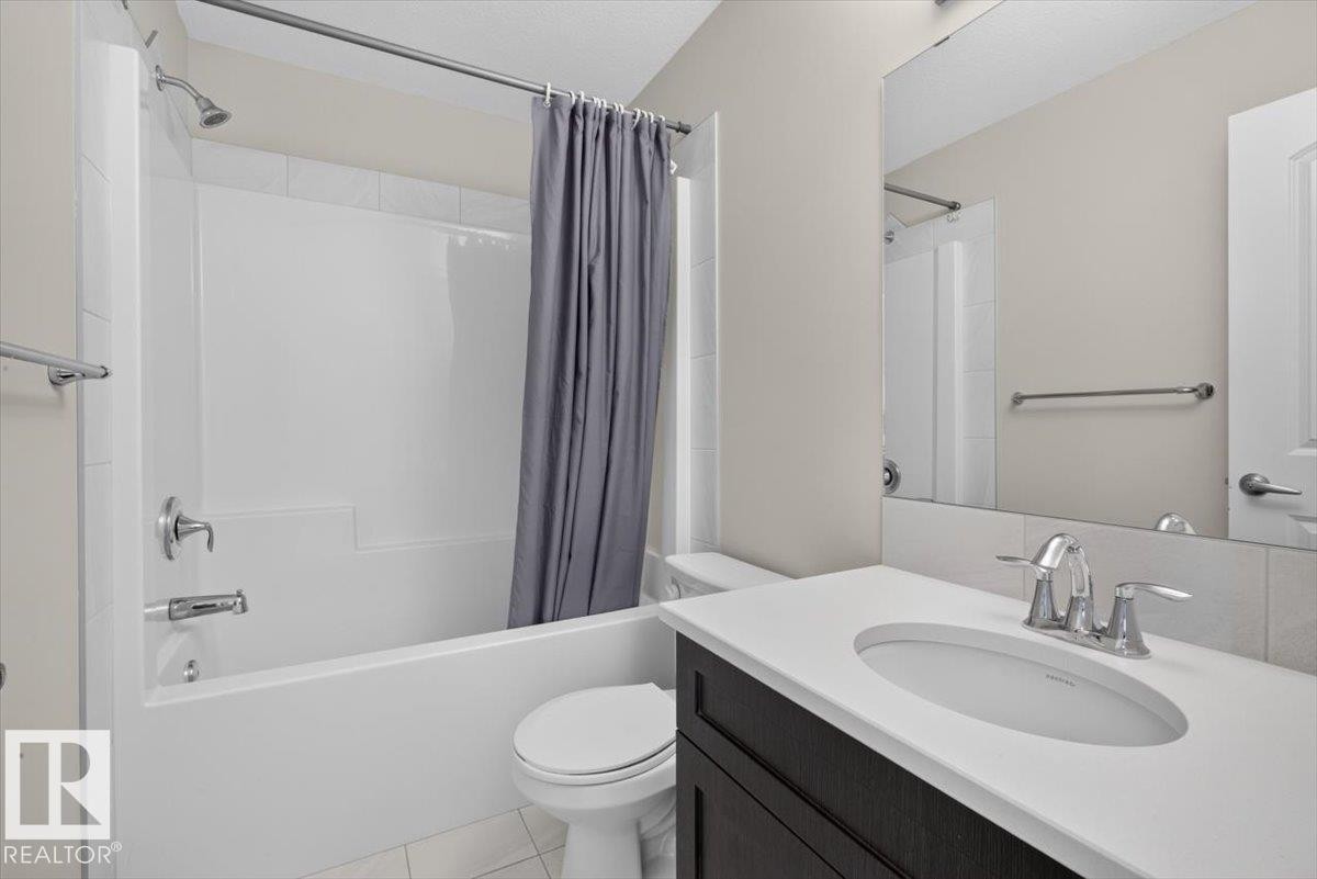 Bathroom featuring a white tub/shower combination with chrome fixtures, a dark wood-finish vanity with a white countertop and integrated sink, and a large wall-mounted mirror - 2144 51 Street, Edmonton, AB