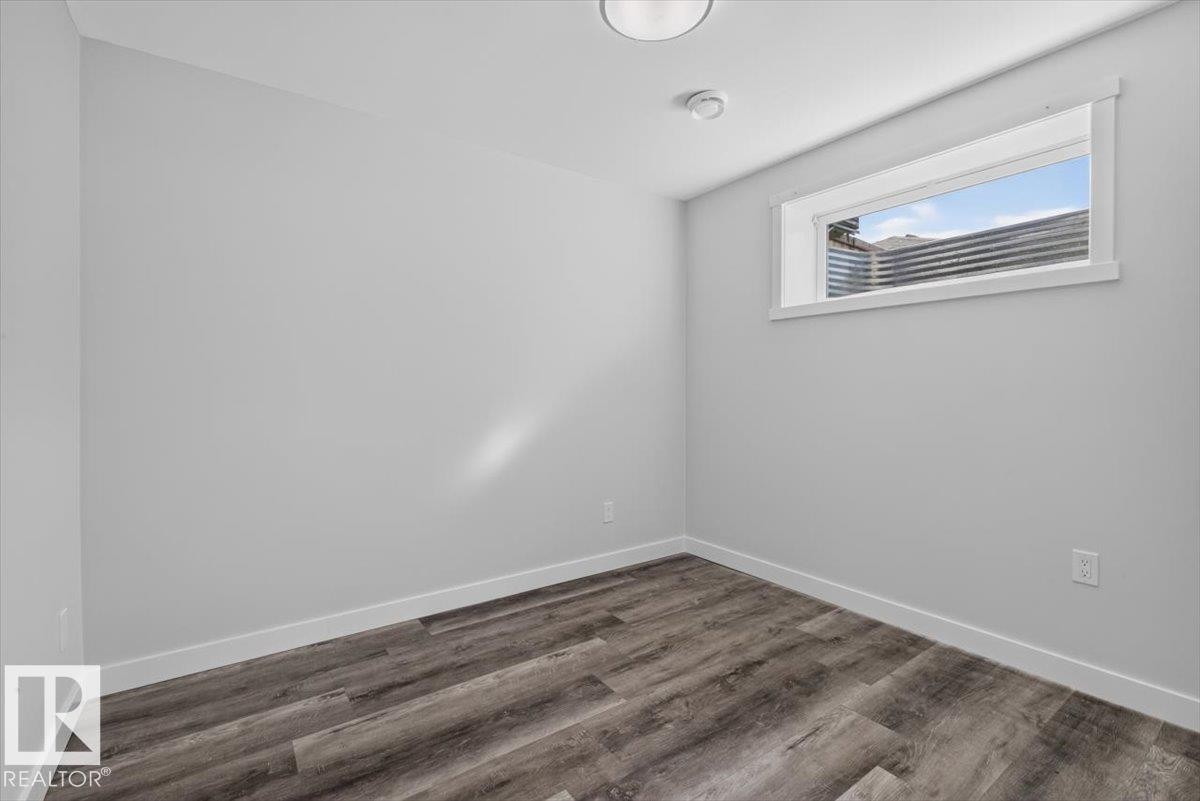 Room featuring neutral-toned walls, wood-finish flooring, white baseboards, and a window with a white frame - 2144 51 Street, Edmonton, AB