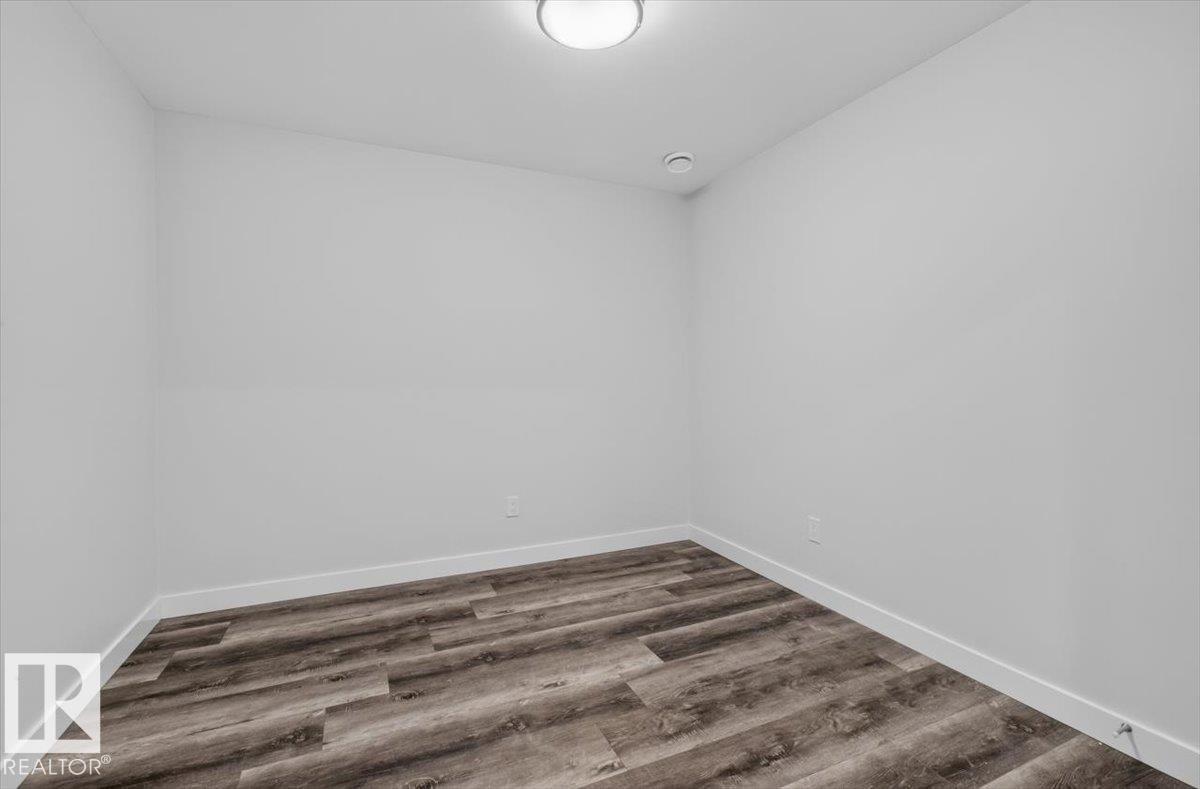 Neutral white walls featuring wood-finish flooring, white baseboards, and a flush-mount ceiling light - 2144 51 Street, Edmonton, AB