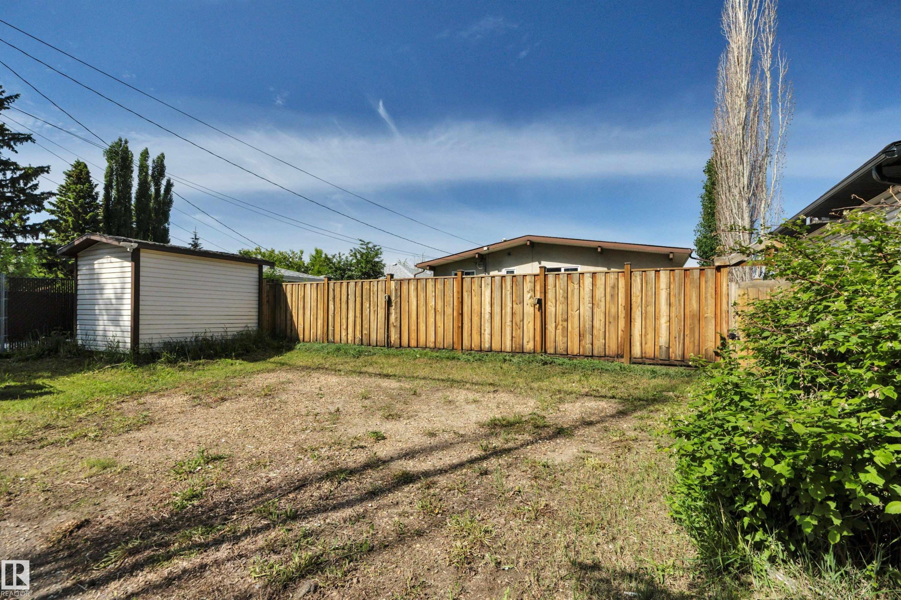 Spacious rear yard featuring a privacy fence, detached storage shed, and established perimeter shrubbery - 9835 74 Street, Edmonton, AB