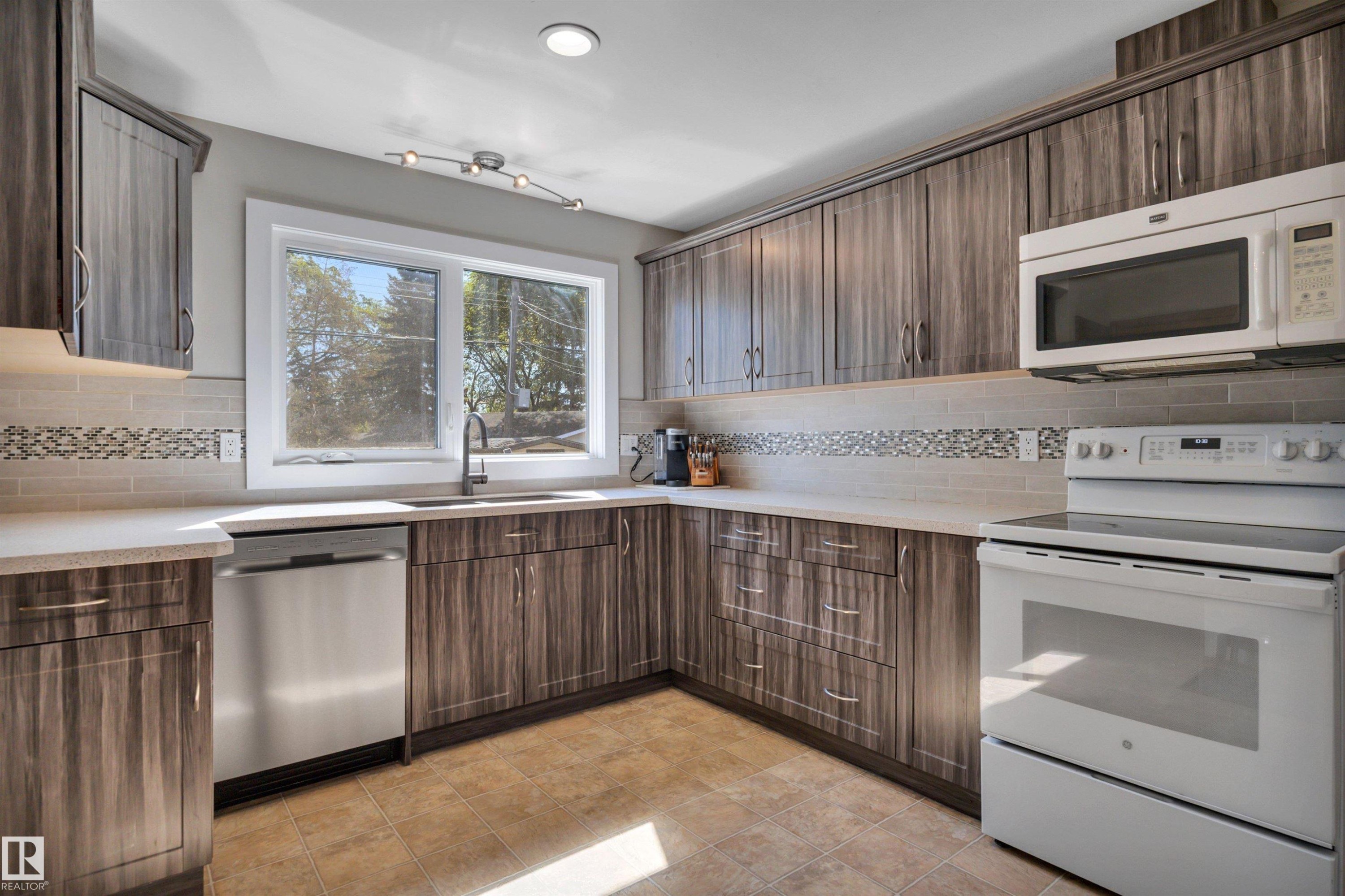 Modern kitchen featuring wood-finish cabinetry and light-toned countertops - 9835 74 Street, Edmonton, AB