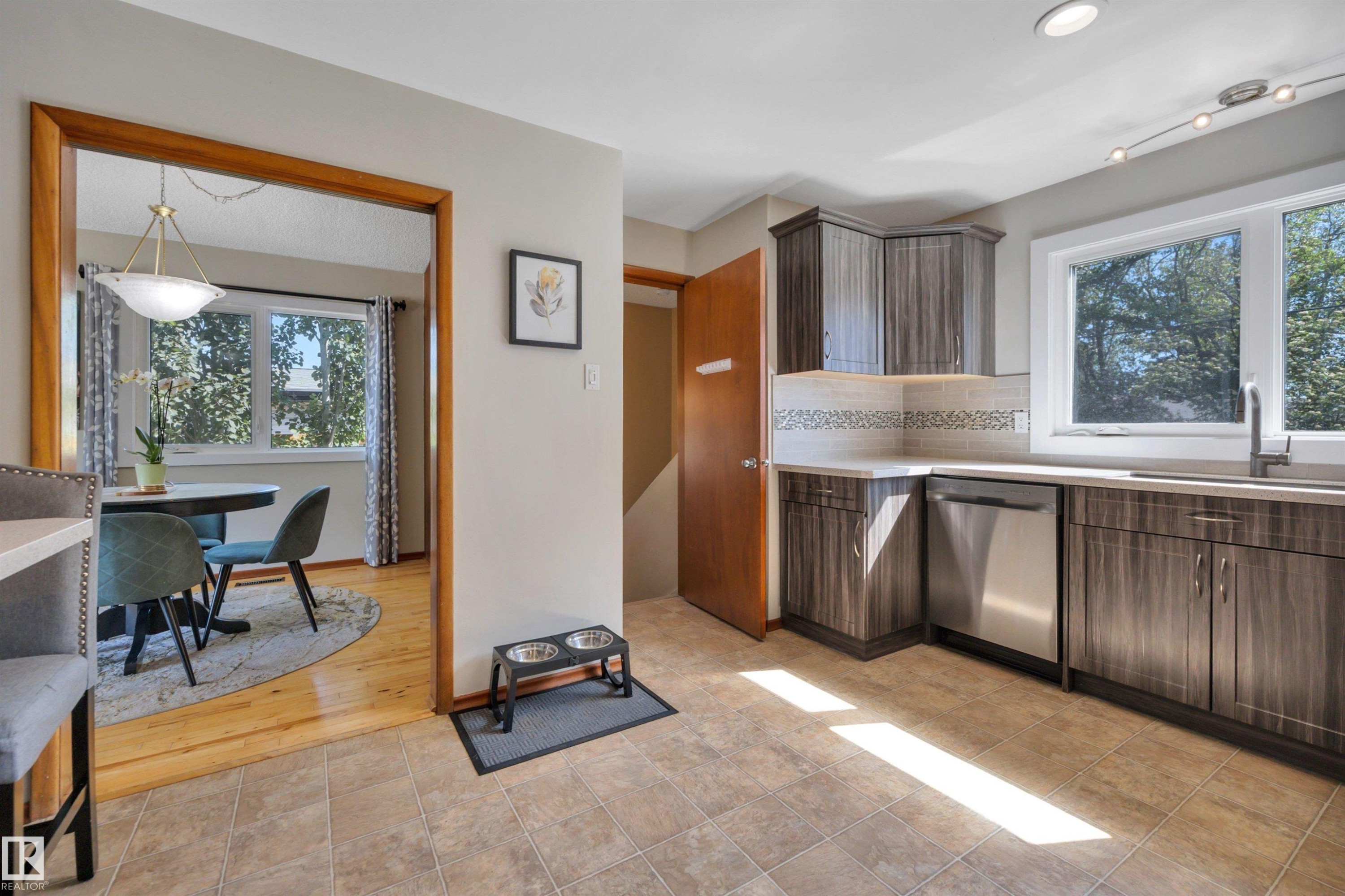 Kitchen featuring tile flooring, wood-finish cabinetry, stainless steel dishwasher, light-toned countertops, and a mosaic tile backsplash - 9835 74 Street, Edmonton, AB