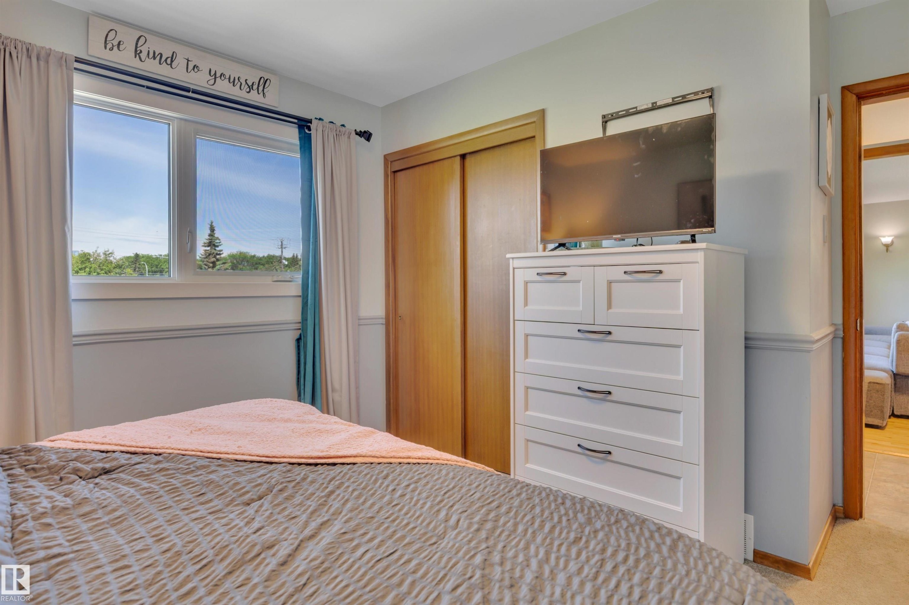 Bedroom featuring a dual-pane window, wood-finish closet doors, and light-toned walls with wainscoting - 9835 74 Street, Edmonton, AB