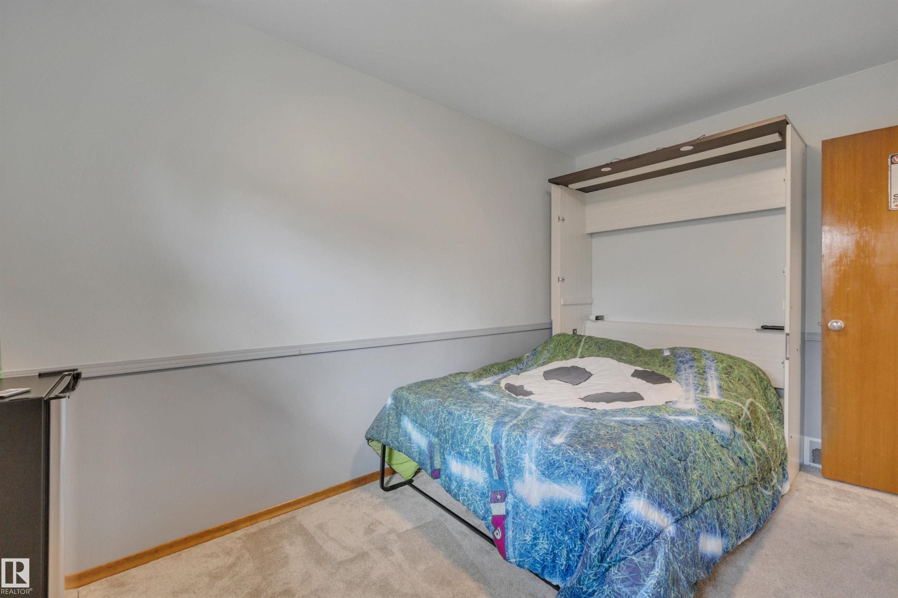 Recessed wall bed with integrated lighting, wood-finish door, light gray walls, white baseboard trim, and light-toned carpet flooring - 9835 74 Street, Edmonton, AB