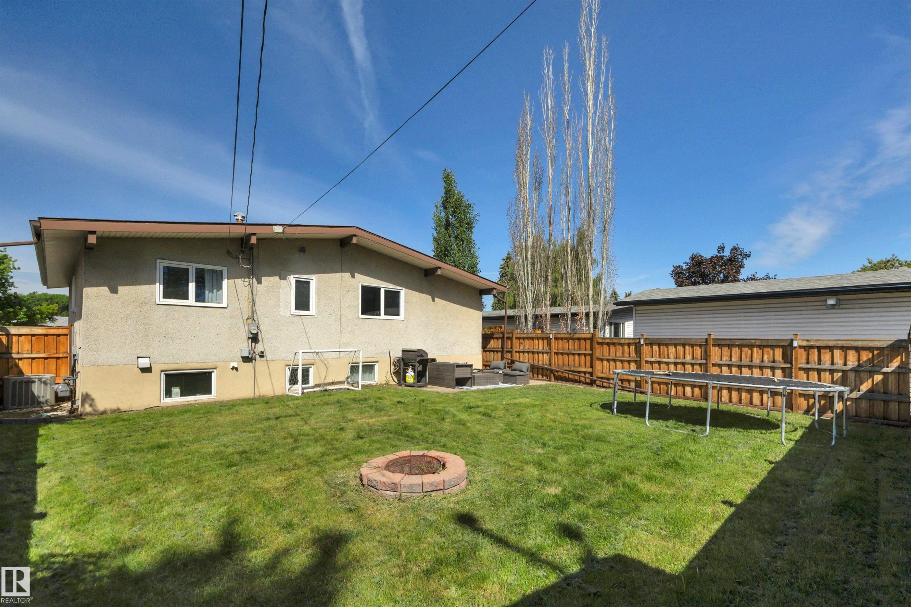 Expansive backyard featuring a manicured lawn, a brick-lined fire pit, and a full-height wood privacy fence - 9835 74 Street, Edmonton, AB