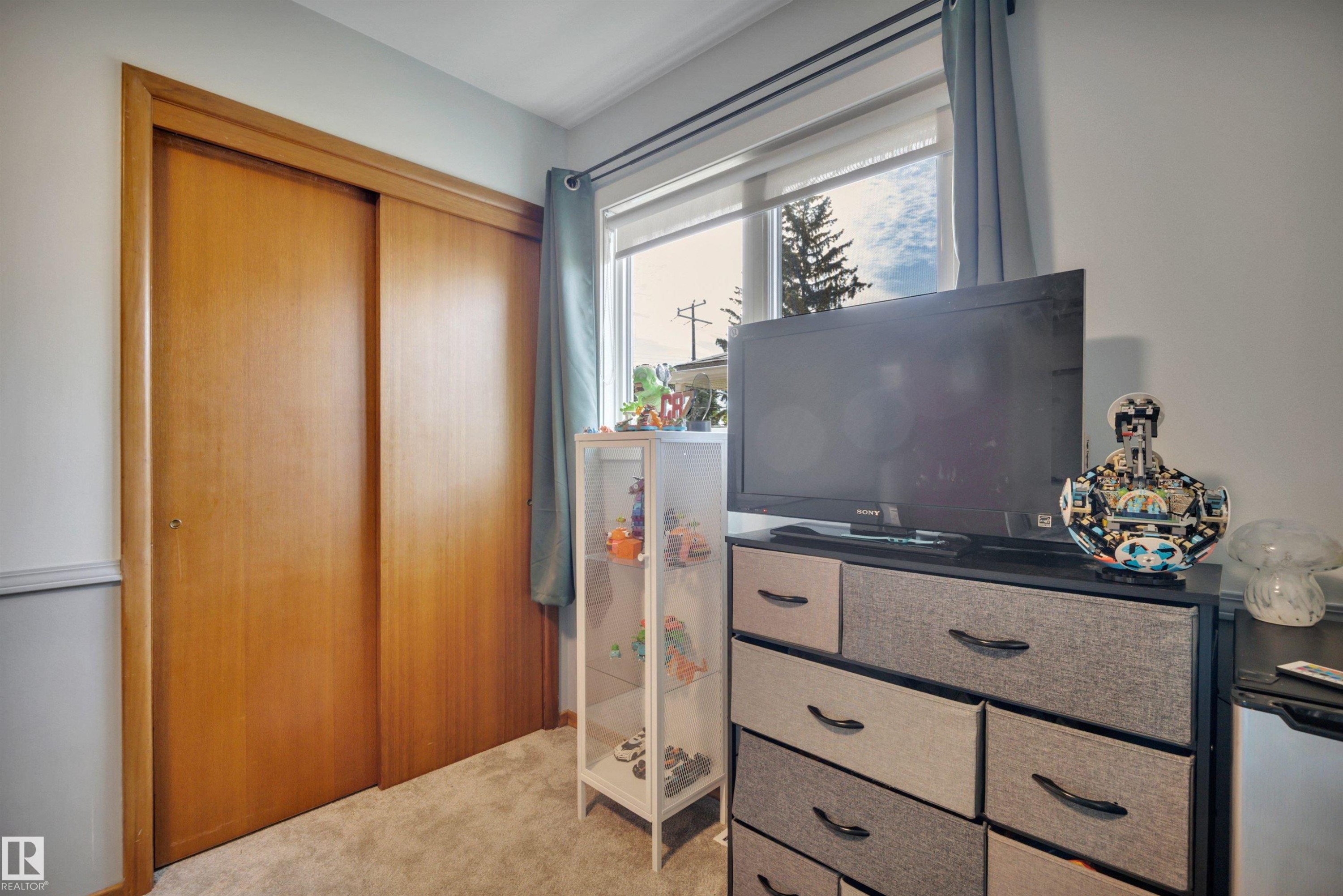 Interior room featuring a window with natural light, neutral wall colors, and a sliding door closet with wood-finish doors - 9835 74 Street, Edmonton, AB