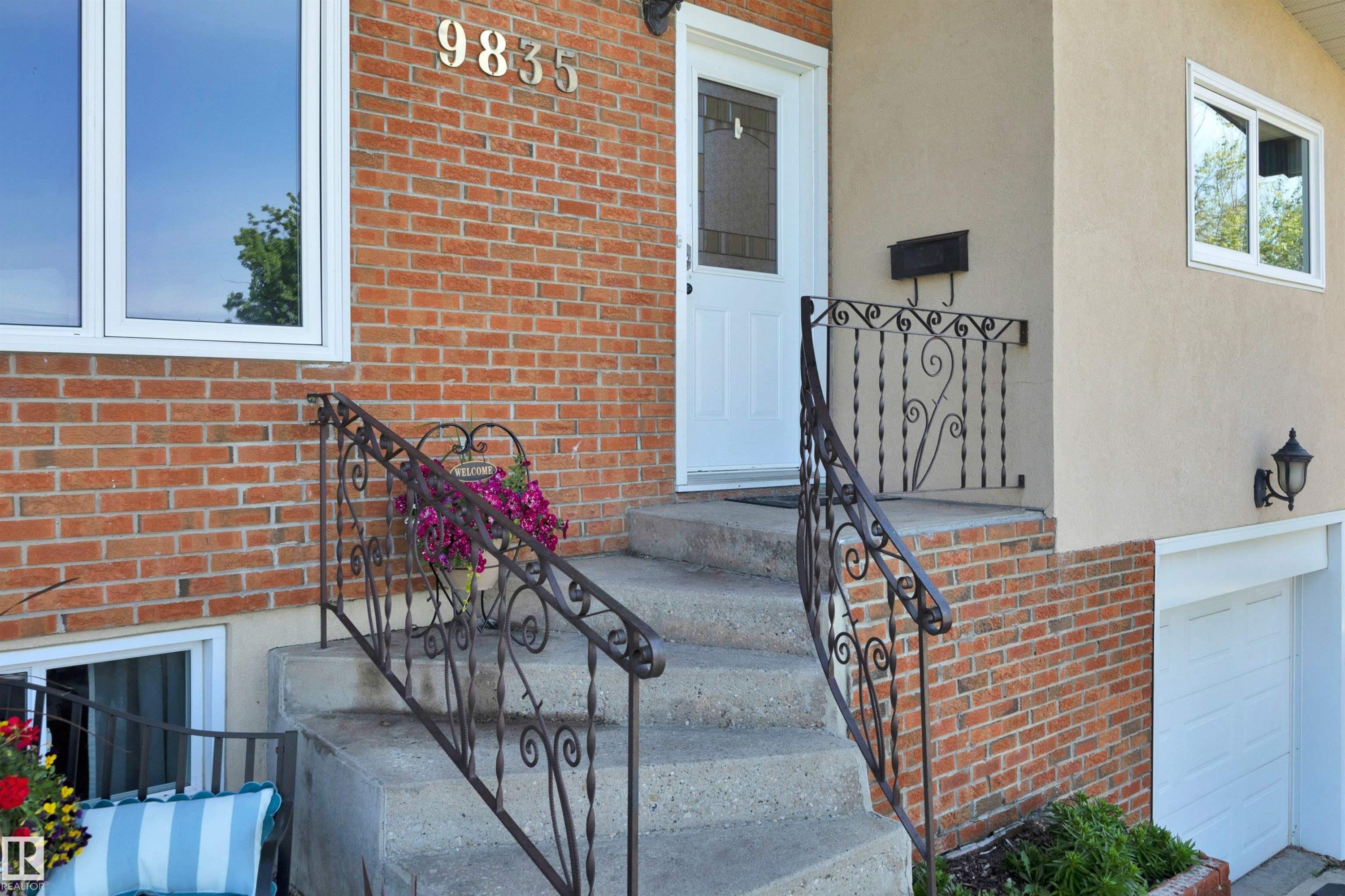 Front entrance featuring concrete steps with decorative wrought iron railings, brick facade, stucco siding, and a white entry door with a privacy screen insert - 9835 74 Street, Edmonton, AB