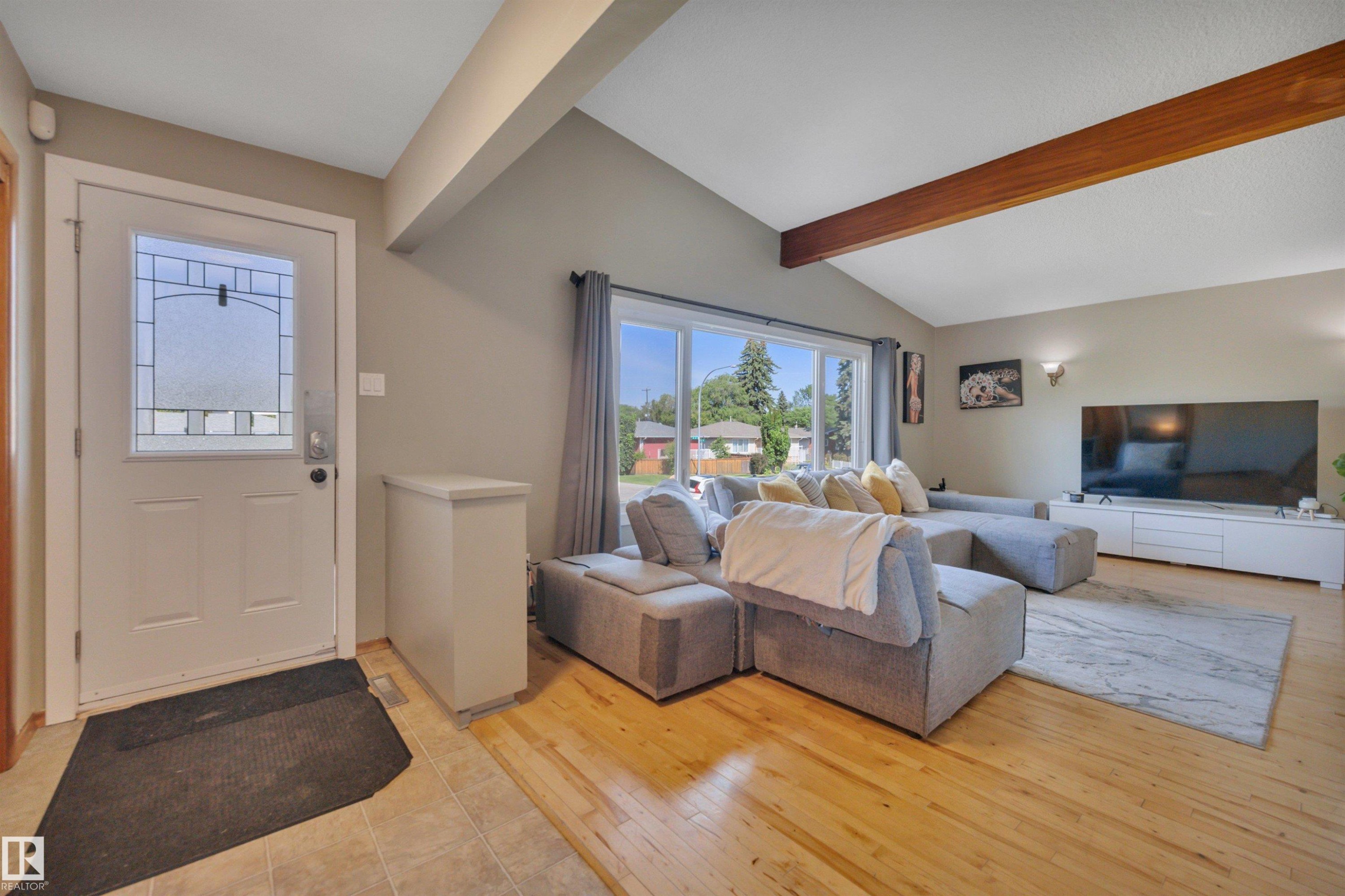 Entryway featuring a white door with decorative glass inserts, opening into a living area with vaulted ceilings and exposed wood beams - 9835 74 Street, Edmonton, AB