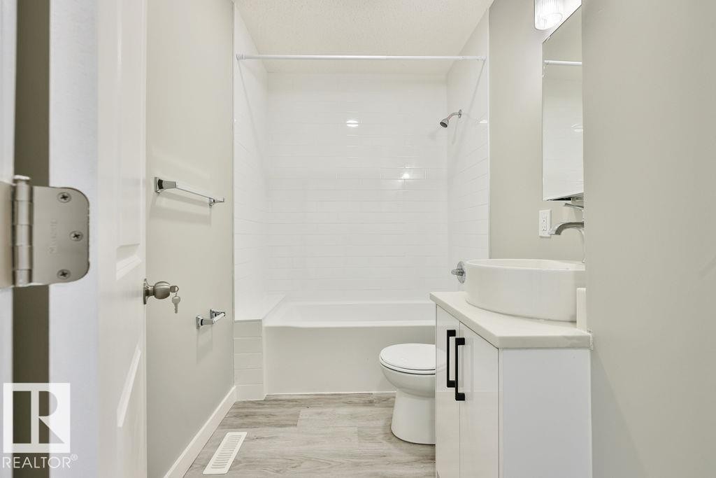 Bathroom featuring a white subway tile tub surround, white bathtub, and wood-finish flooring - 11241 88 Street, Edmonton, AB