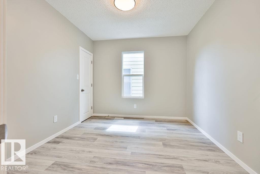Room featuring light gray walls, wood-finish flooring, a white trim package, and an overhead flush-mount light fixture - 11241 88 Street, Edmonton, AB