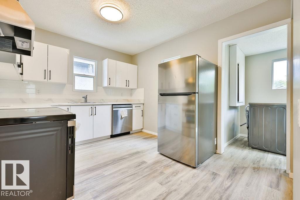 Modern kitchen featuring wood-finish flooring, white cabinetry with dark pulls, stainless steel appliances, and a light-toned backsplash - 11241 88 Street, Edmonton, AB