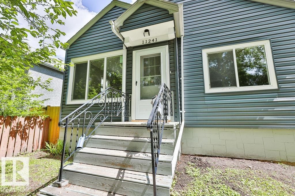 Exterior featuring horizontal siding, a white entry door, and decorative wrought iron railings - 11241 88 Street, Edmonton, AB