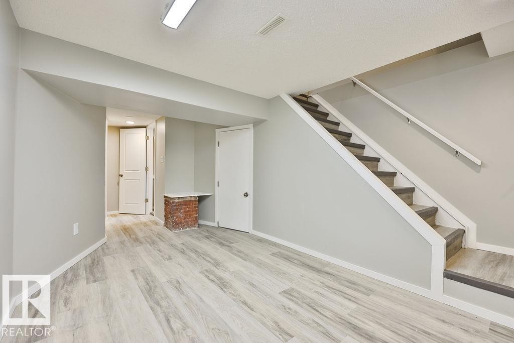 Finished lower level with light wood-finish flooring, light gray wall paint, white trim, and a carpeted staircase with white handrails - 11241 88 Street, Edmonton, AB