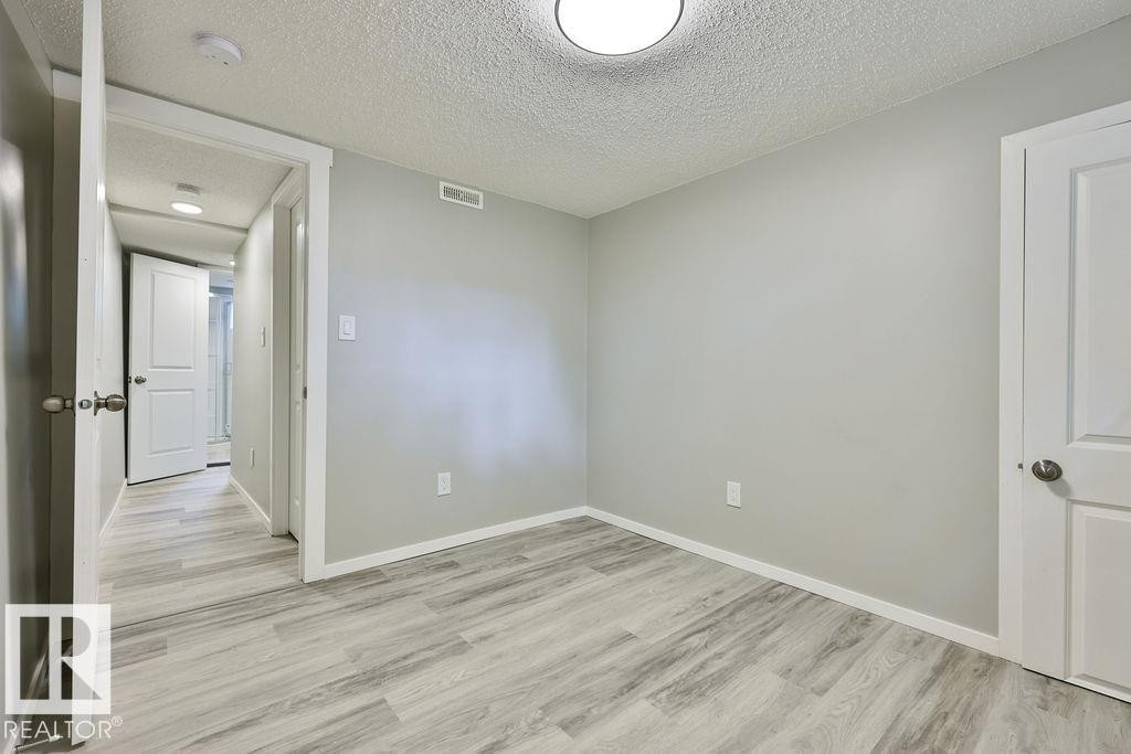 Room featuring light gray walls, wood-finish flooring, white trim, and a flush-mount ceiling light - 11241 88 Street, Edmonton, AB
