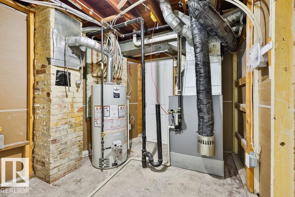 Utility area featuring a water heater, furnace, exposed ductwork, brick support column, and concrete flooring - 11241 88 Street, Edmonton, AB