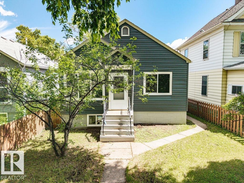Exterior featuring horizontal siding, white trim windows, a central entry door with storm door, and a picket fence - 11241 88 Street, Edmonton, AB