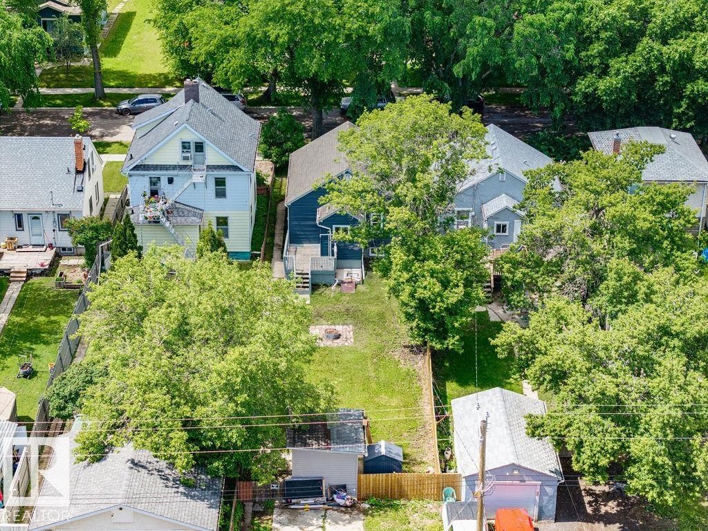 Expansive backyard featuring a green lawn, mature trees, and a detached garage with an orange door - 11241 88 Street, Edmonton, AB