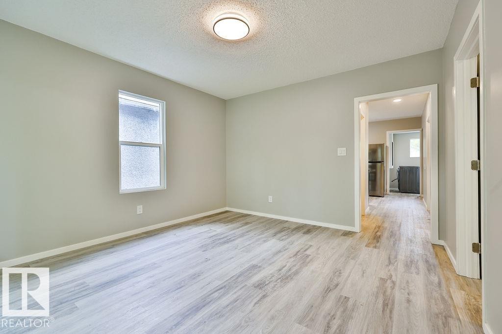 Spacious room featuring wood-finish flooring, light gray wall paint, and a single window with white trim - 11241 88 Street, Edmonton, AB