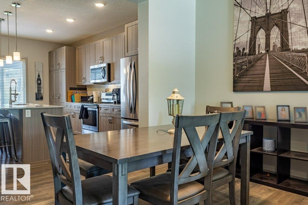 Open-concept kitchen and dining area featuring wood-finish flooring, recessed lighting, and a kitchen island with pendant lighting - 17123 49 Street, Edmonton, AB