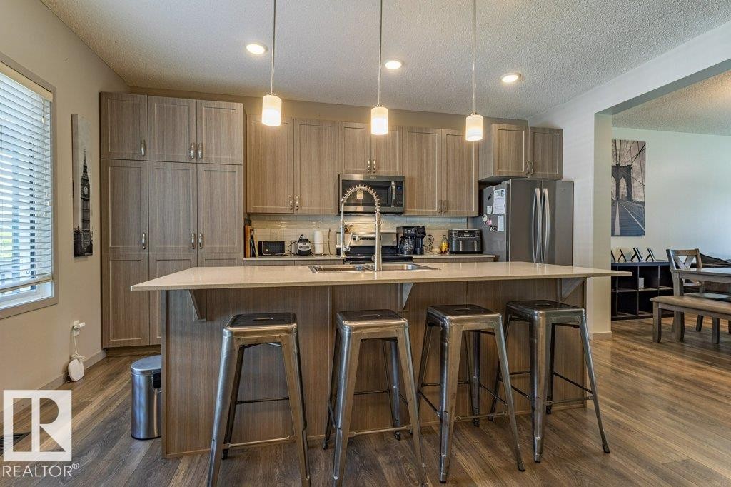 Kitchen featuring a central island with countertop seating, stainless steel appliances, wood-finish flooring, recessed lighting, and pendant lighting fixtures - 17123 49 Street, Edmonton, AB