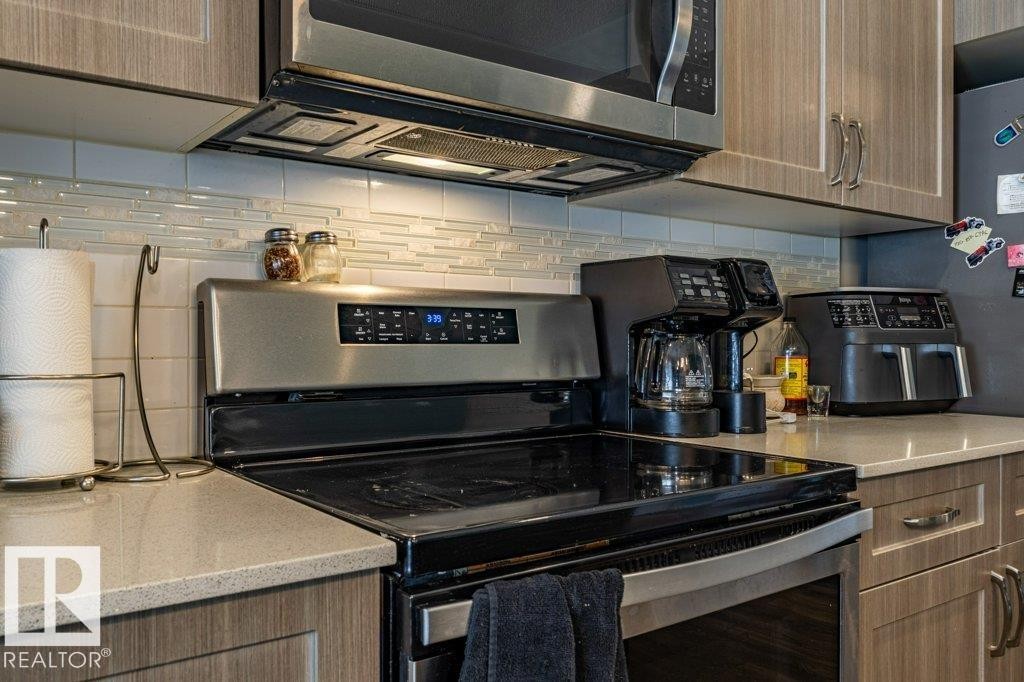 Stainless steel electric range with built-in microwave, light wood-finish cabinetry, light-toned countertops, and a stacked tile backsplash - 17123 49 Street, Edmonton, AB