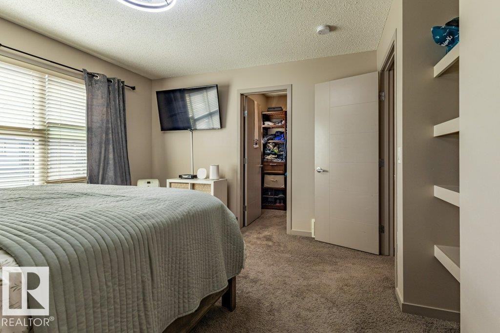 Carpeted interior space featuring a window with horizontal blinds and a privacy curtain, a built-in closet with shelving, a modern ceiling light fixture, and wall-mounted shelving - 17123 49 Street, Edmonton, AB