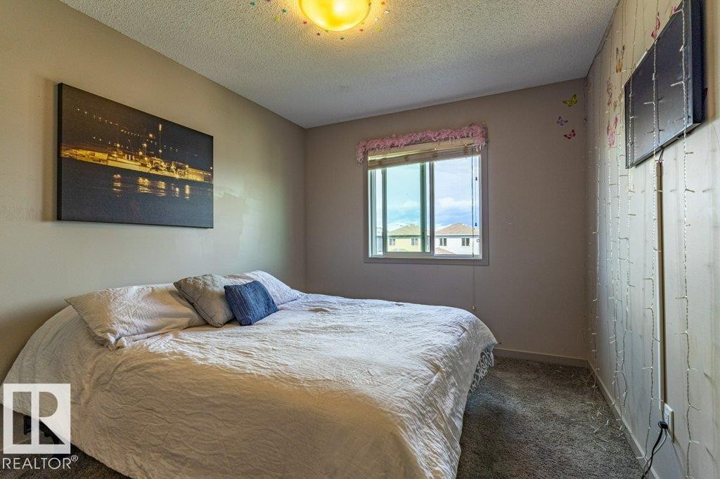 Carpeted bedroom featuring a large window, neutral wall paint, and a textured wall panel accent - 17123 49 Street, Edmonton, AB