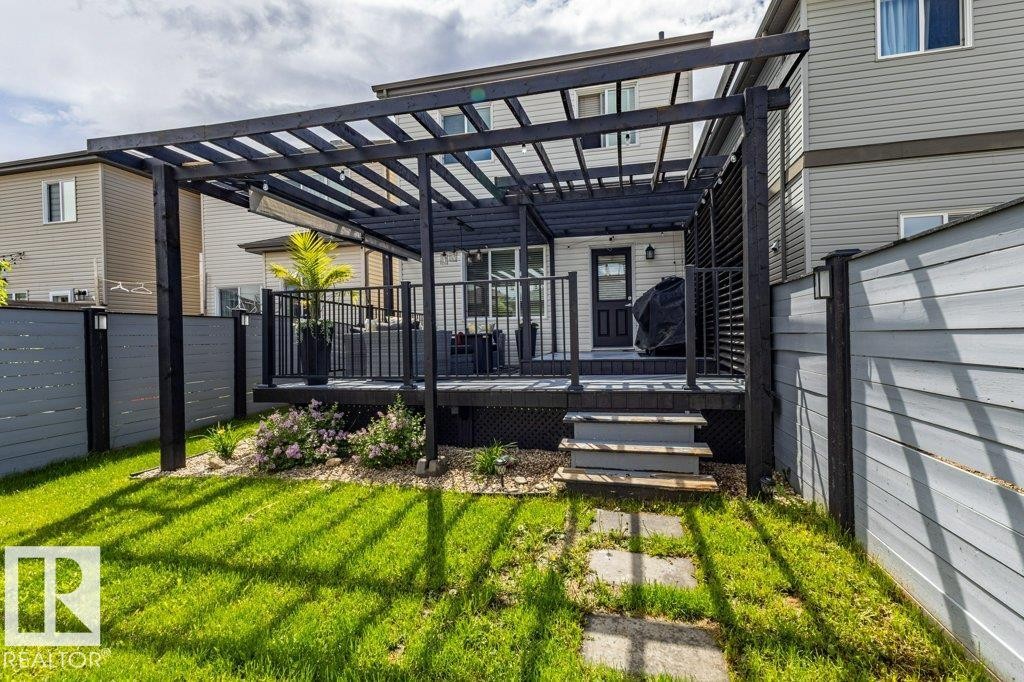 Expansive backyard featuring a manicured lawn, stone pathway, and a multi-level deck with a contemporary dark-stained pergola - 17123 49 Street, Edmonton, AB