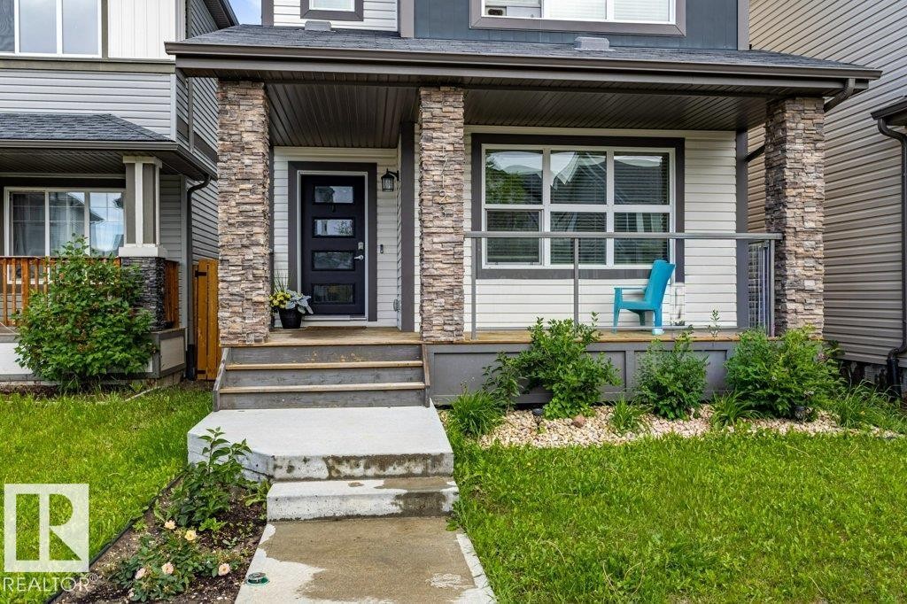 Inviting front porch featuring stone-clad pillars, a modern dark-paneled door with frosted glass inserts, and a coordinating dark gray porch railing - 17123 49 Street, Edmonton, AB