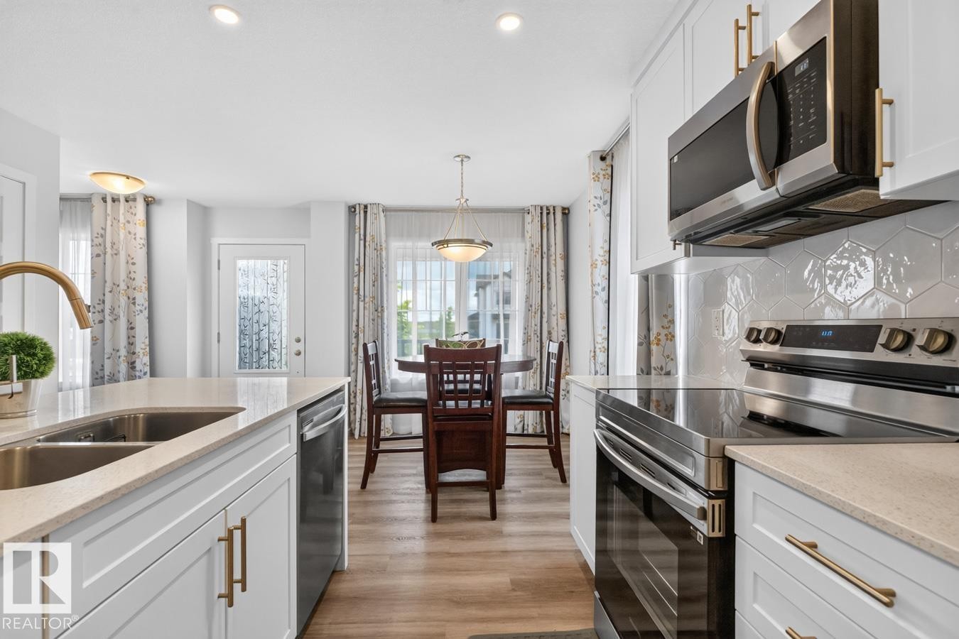 Bright kitchen featuring white cabinetry with gold-tone hardware, stainless steel appliances, and a hexagonal tile backsplash - 1022 Hearthstone Boulevard, Sherwood Park, AB