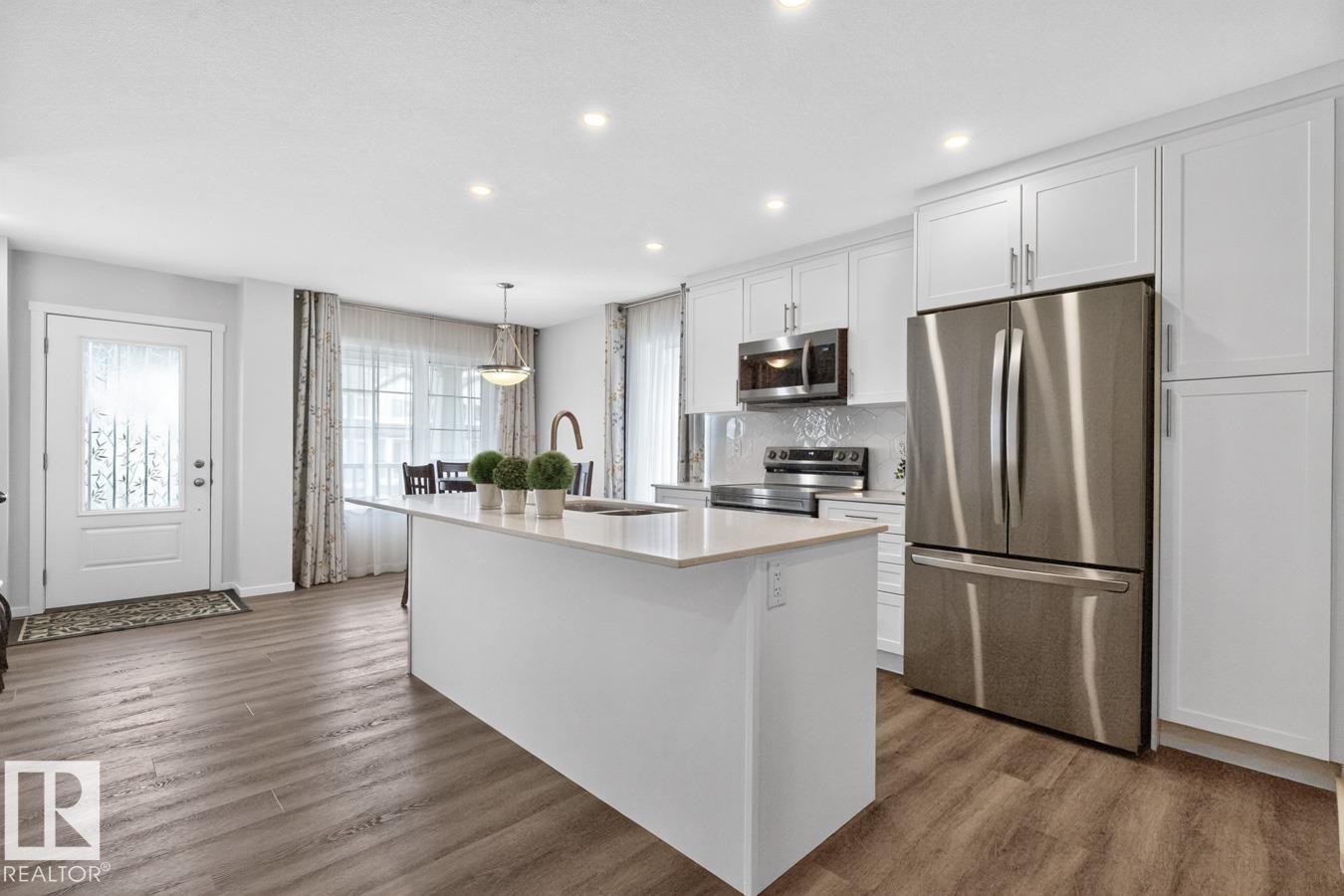 Contemporary kitchen featuring a large island with a light-toned countertop, white cabinetry with silver hardware, and stainless steel appliances - 1022 Hearthstone Boulevard, Sherwood Park, AB