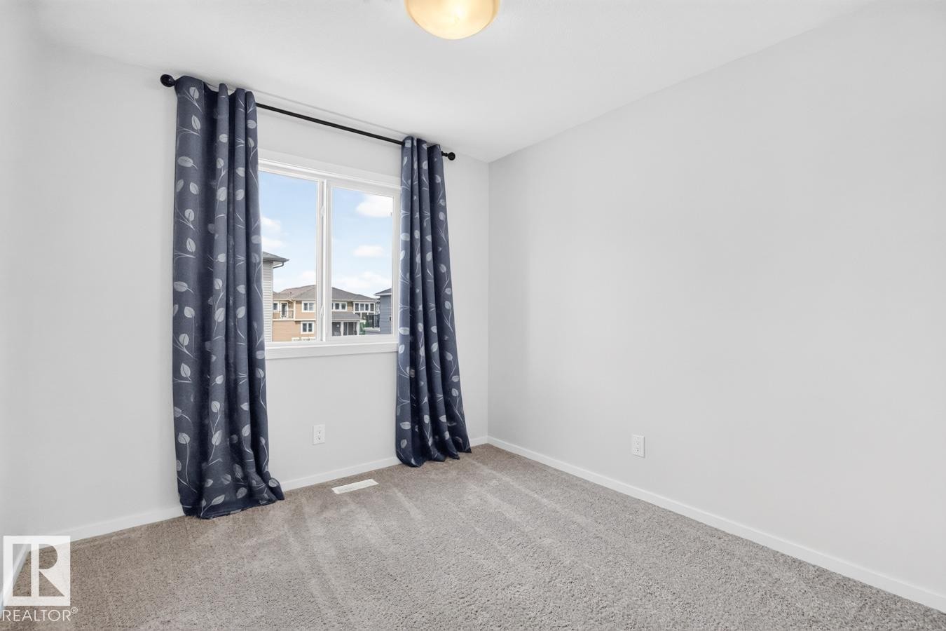 Light-filled room featuring a double window with black hardware, neutral carpeting, and white walls - 1022 Hearthstone Boulevard, Sherwood Park, AB